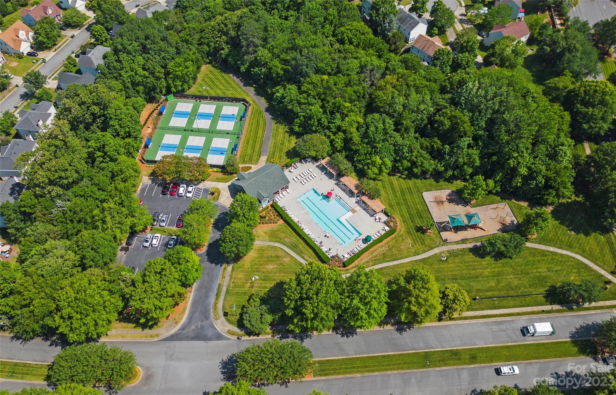 Aerial view of a community recreation area with a swimming pool, pickleball courts, and playground.