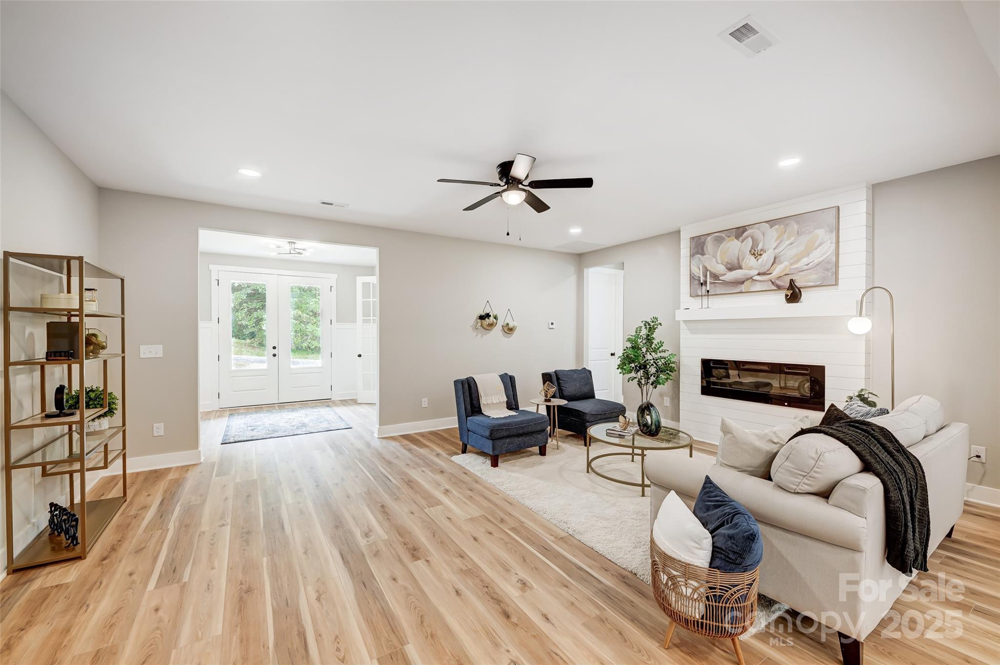 Furnished living room with a white shiplap fireplace, cream sofa, blue chairs, and light wood floors.