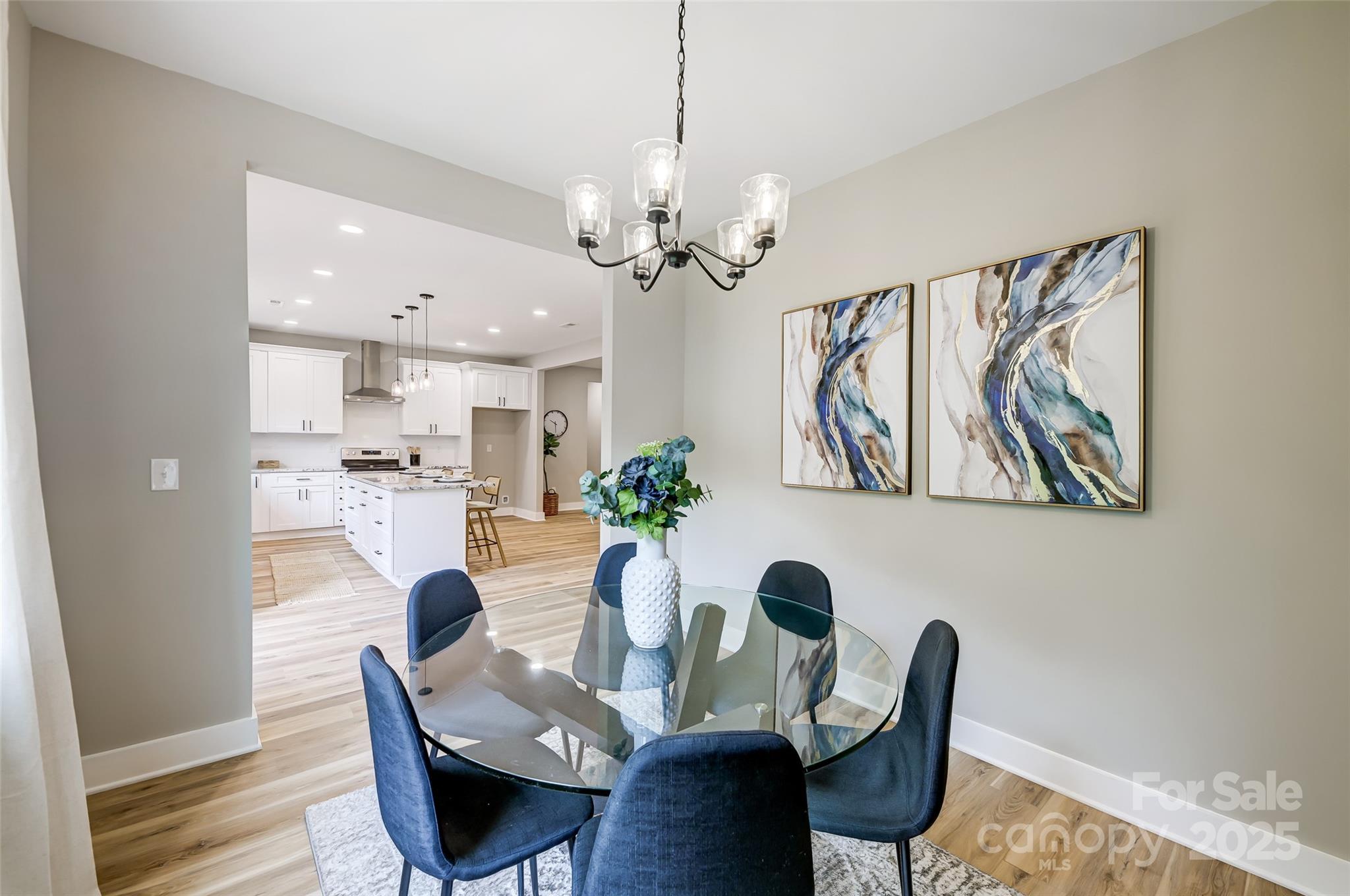 Dining room with a glass table and navy chairs opening onto a bright kitchen with a white island.