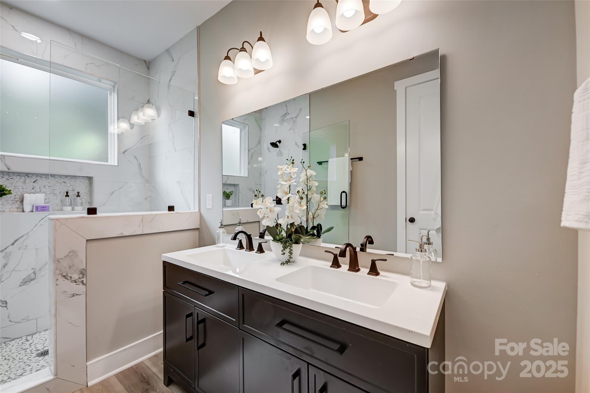Bathroom with a dark vanity, marble-look tile, and glass-enclosed shower.