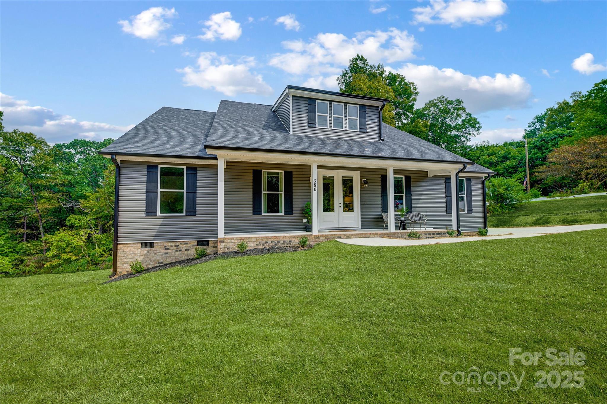 Gray-sided house with a covered front porch, dormer, and broad green lawn.