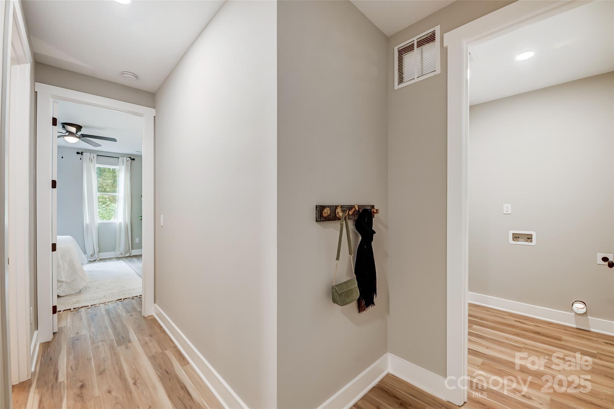 Hallway with wood-look floors, a coat rack, and doorways to a bedroom and laundry room.