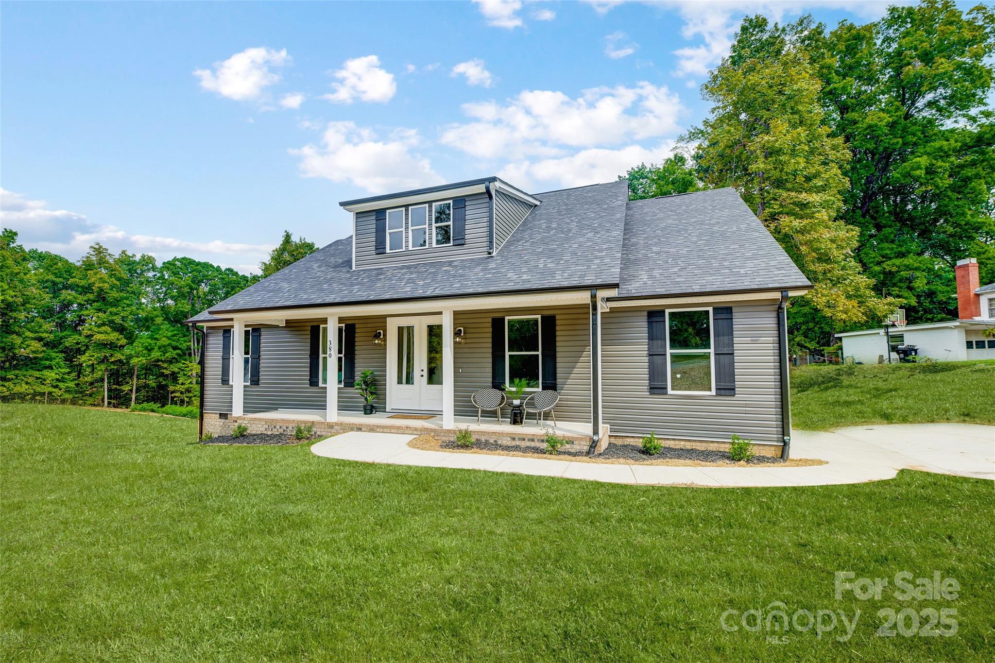Gray house with a covered front porch, upper dormer, and curved walkway across the lawn.