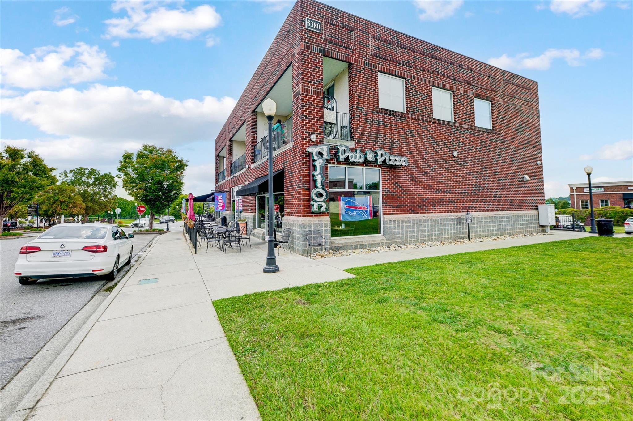 Two-story brick commercial building with storefronts, balconies, and sidewalk patio seating.