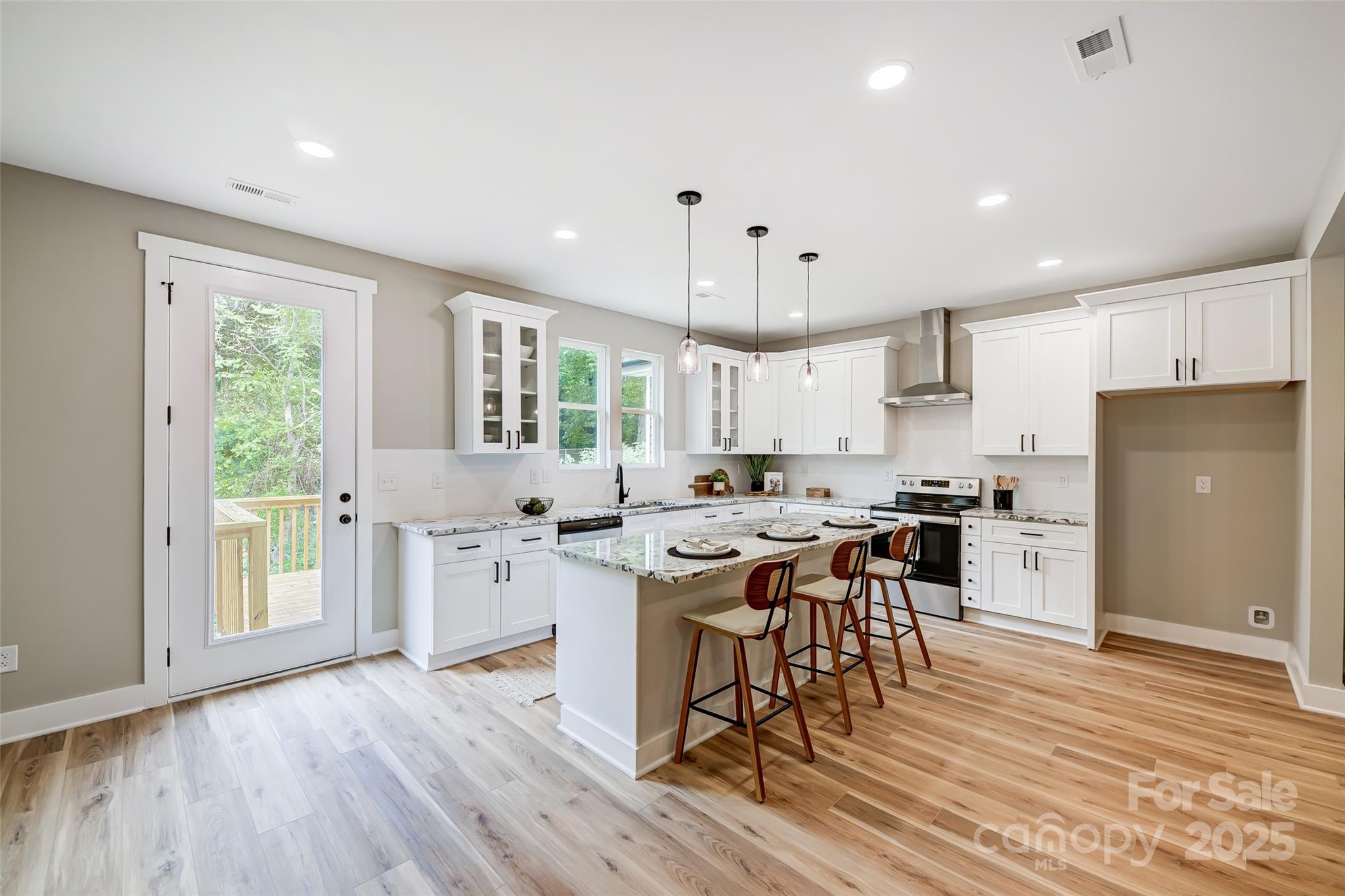 Bright kitchen with white cabinets, a marble-patterned island, three bar stools and a glass deck door.