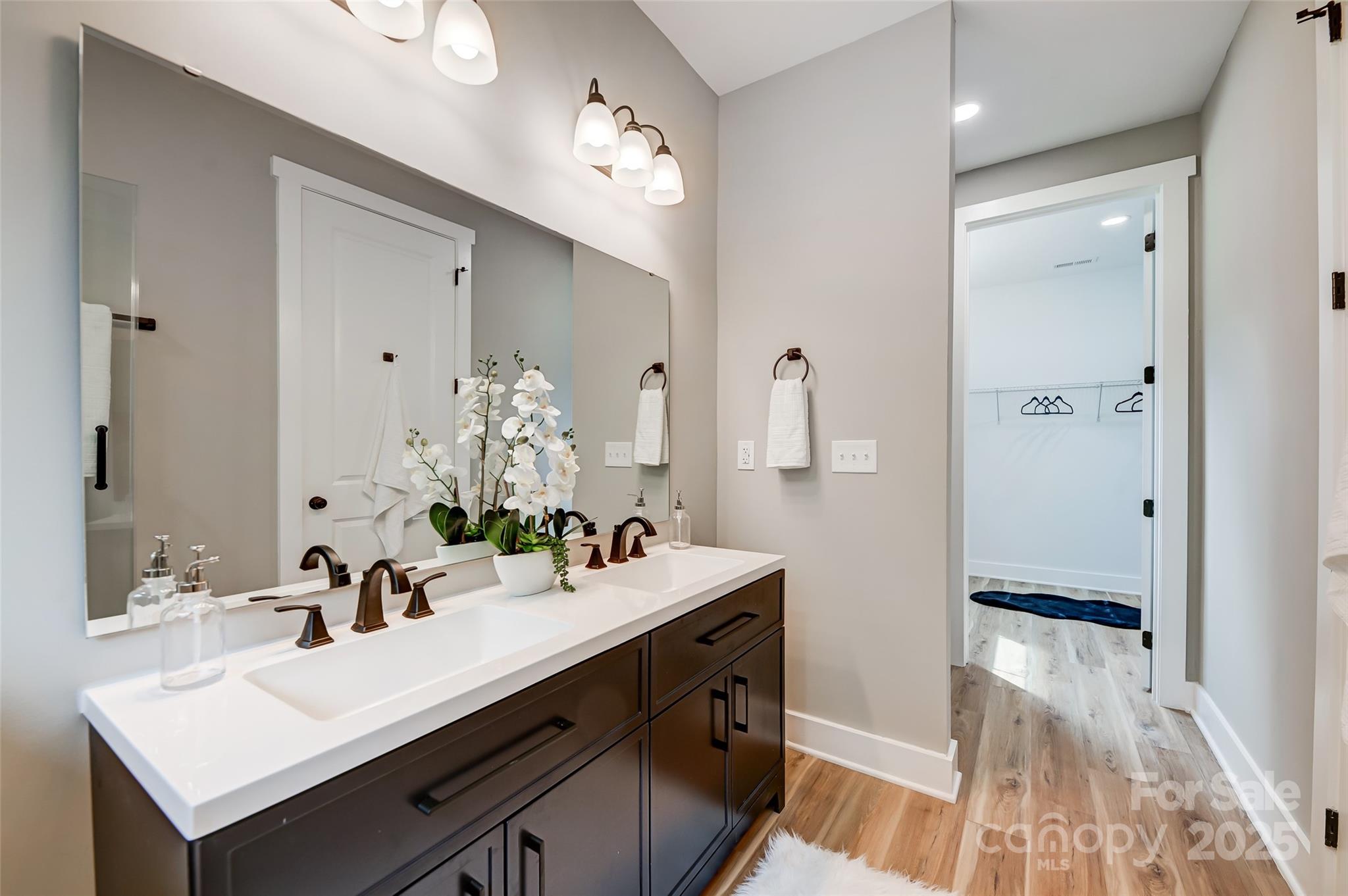 Bathroom with a dark double vanity, two sinks, large mirrors, and an open doorway to a walk-in closet.