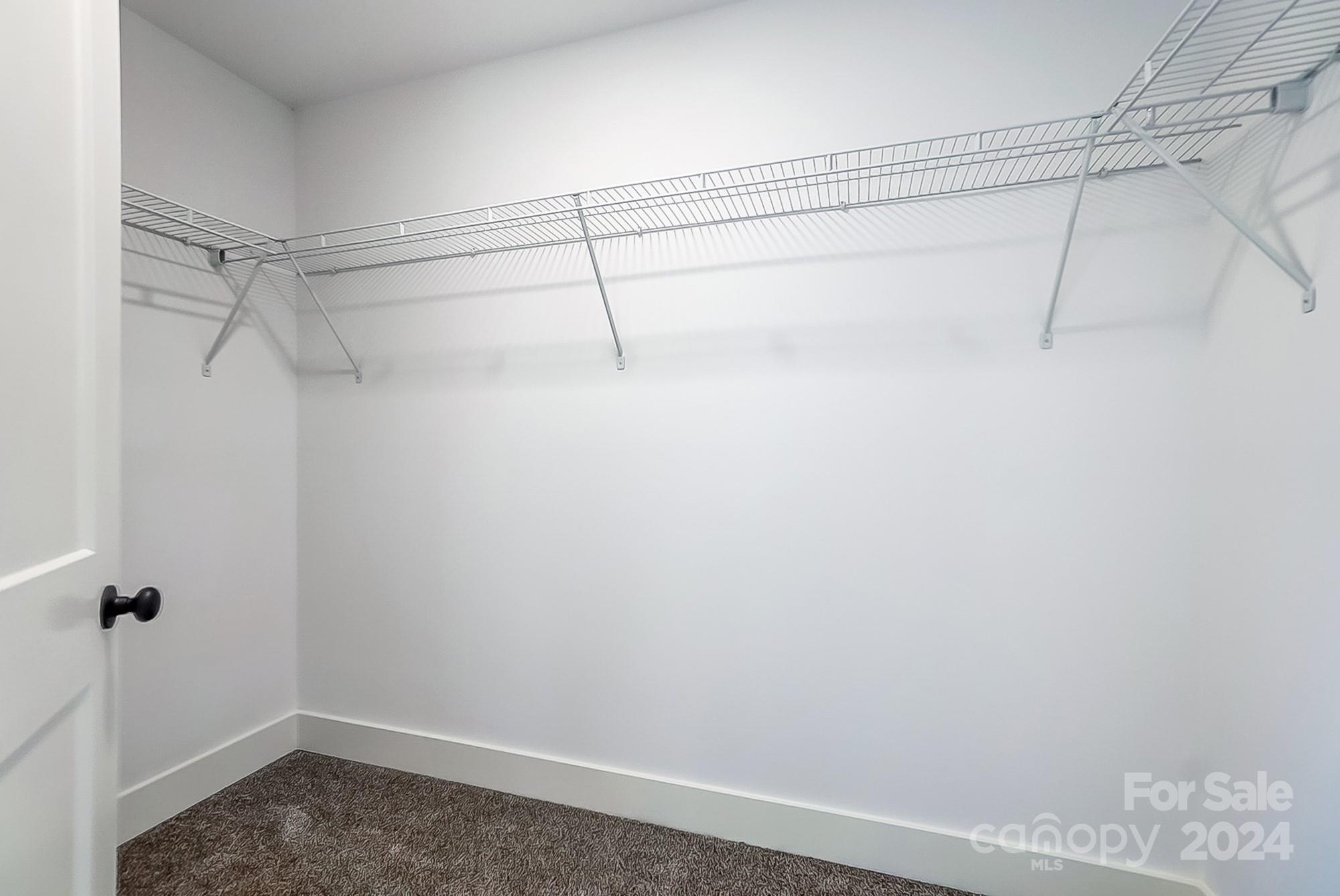 Empty walk-in closet with wraparound wire shelving and brown carpet.