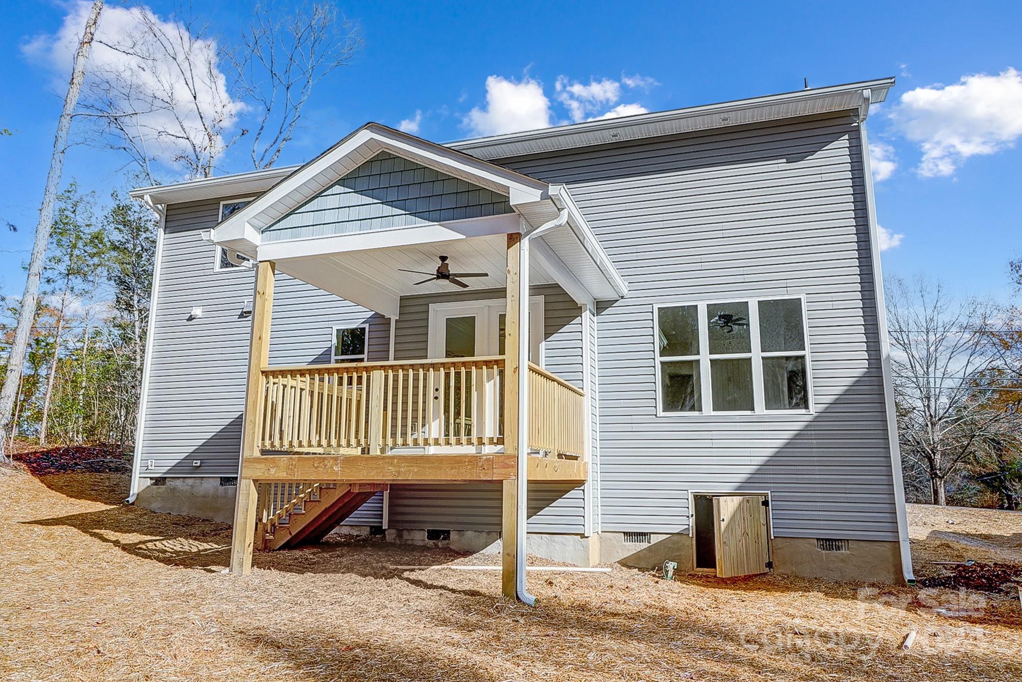 Rear of a gray-sided house with a raised covered wooden deck and stairs.
