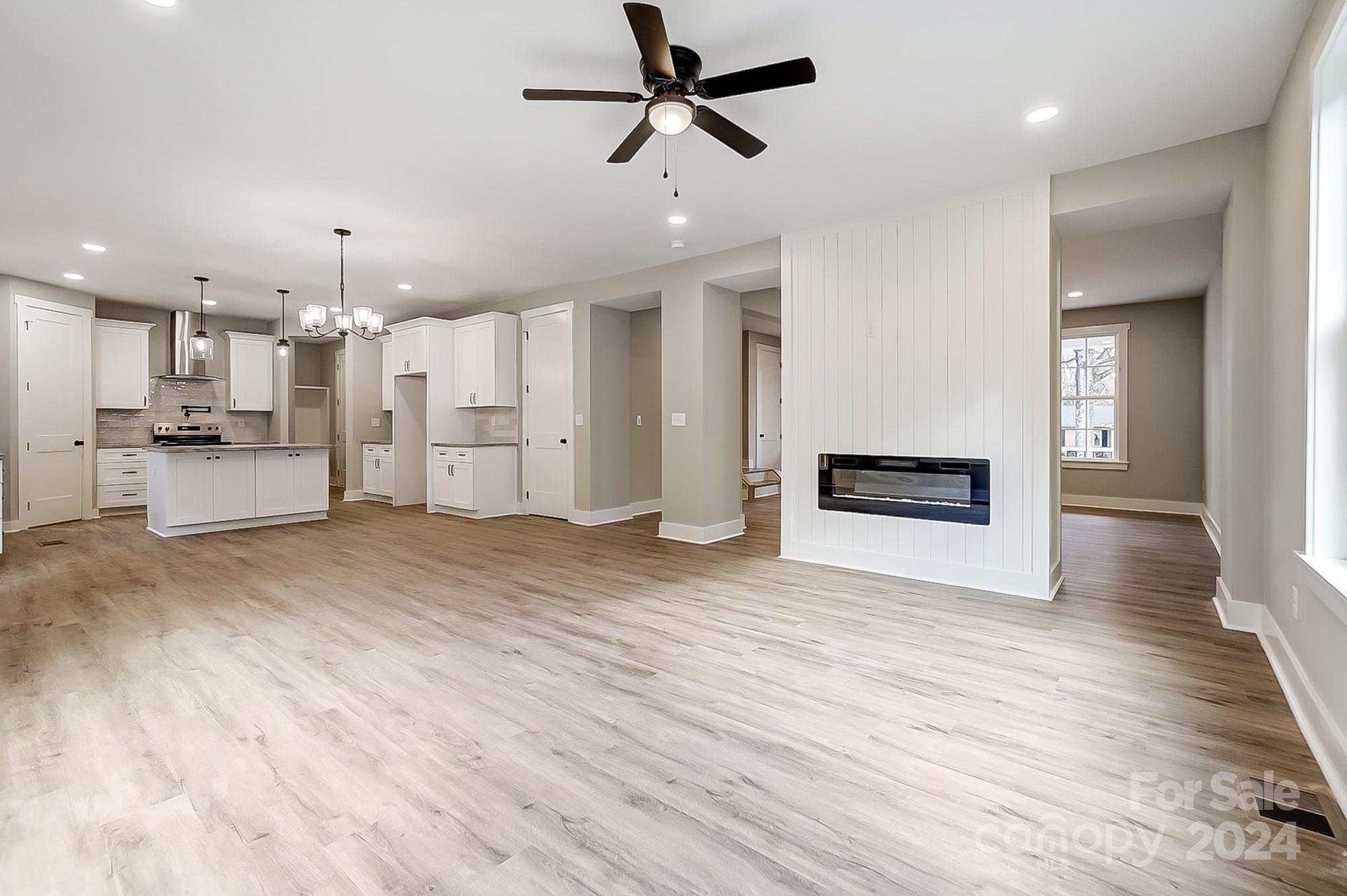 Open-plan kitchen and living room with white cabinets, wood floors, and a fireplace in a paneled divider.