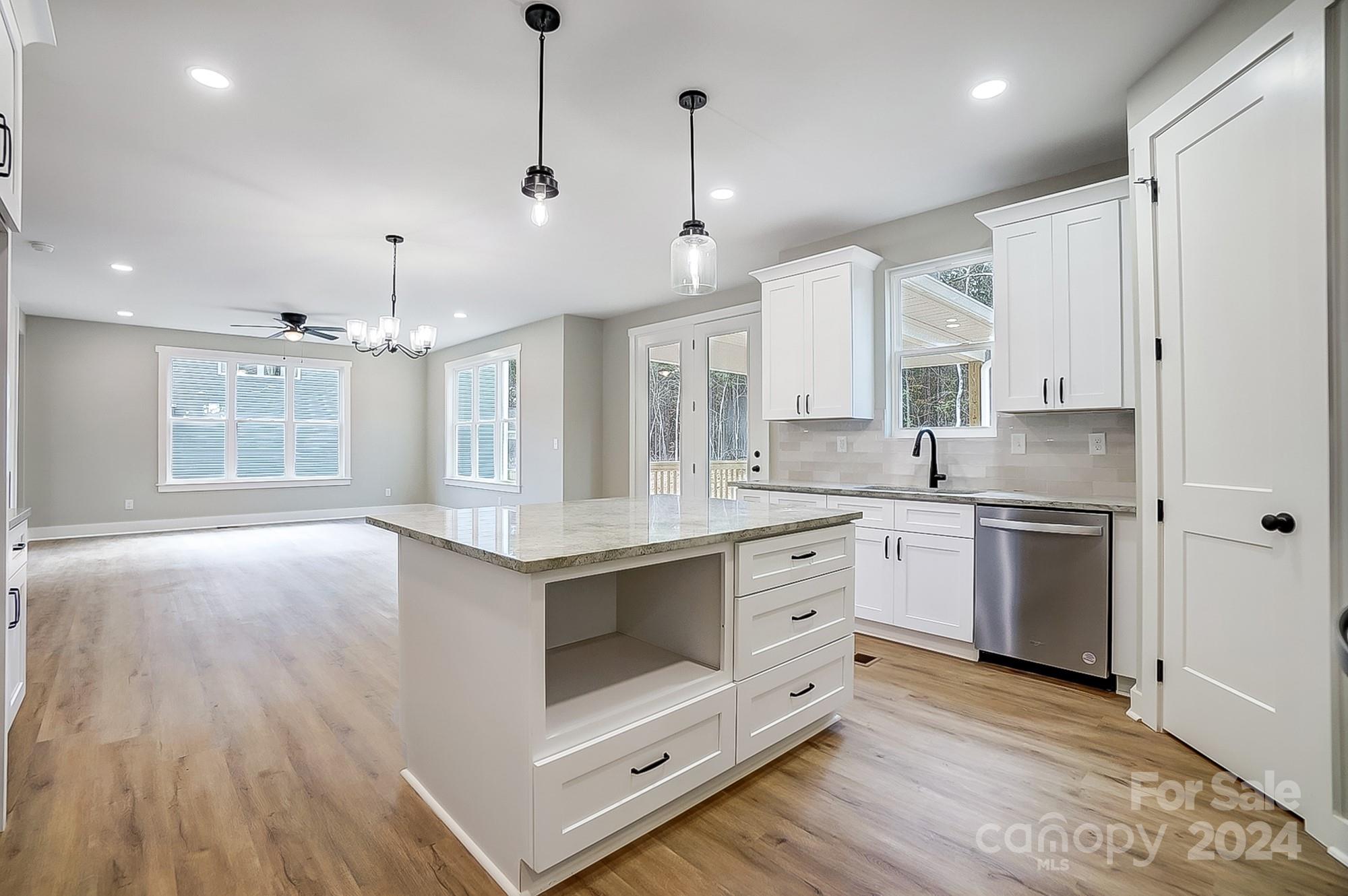 Vacant kitchen with a large stone-topped island, white cabinets, and an open living area.