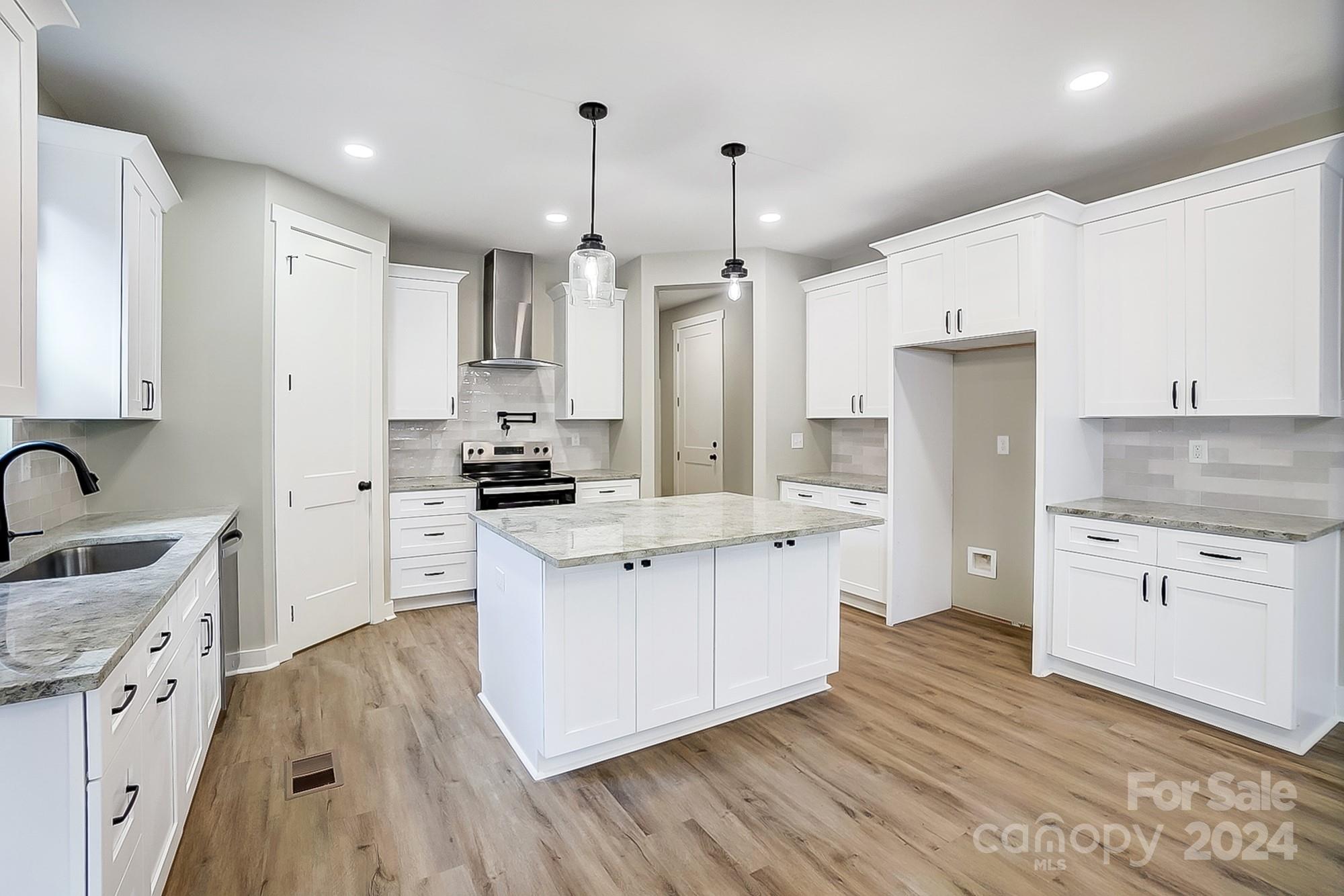 Kitchen with white shaker cabinets, a large granite-topped island, stainless steel range, and wood-look flooring.