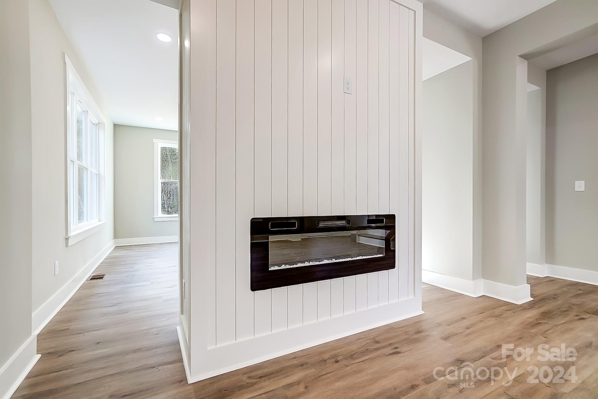Vacant interior with a modern linear fireplace on a white paneled wall and wood-look floors.