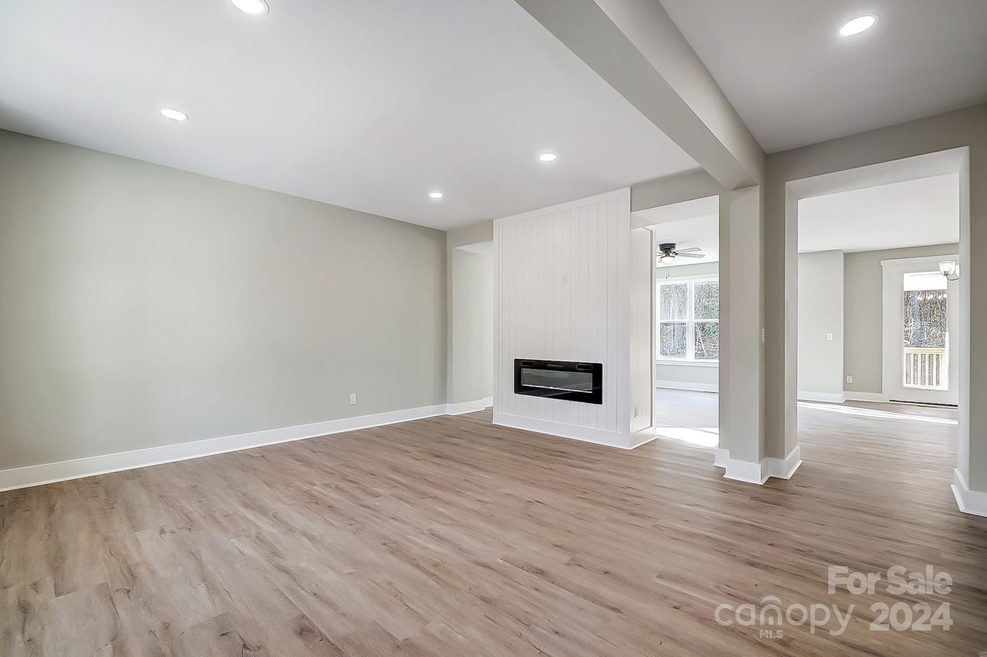 Empty living room with wood-look floors and a built-in fireplace in a paneled partition.