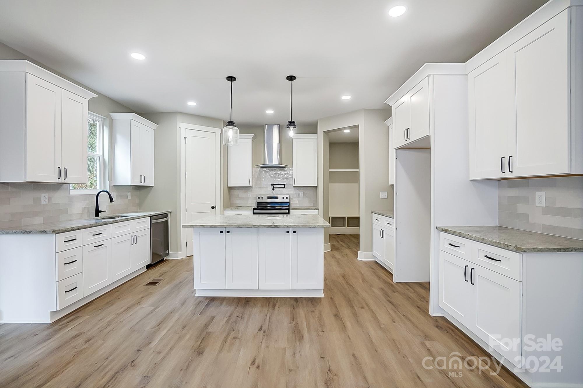 Bright kitchen with white cabinets, central island, stainless steel range, and wood-look floors.