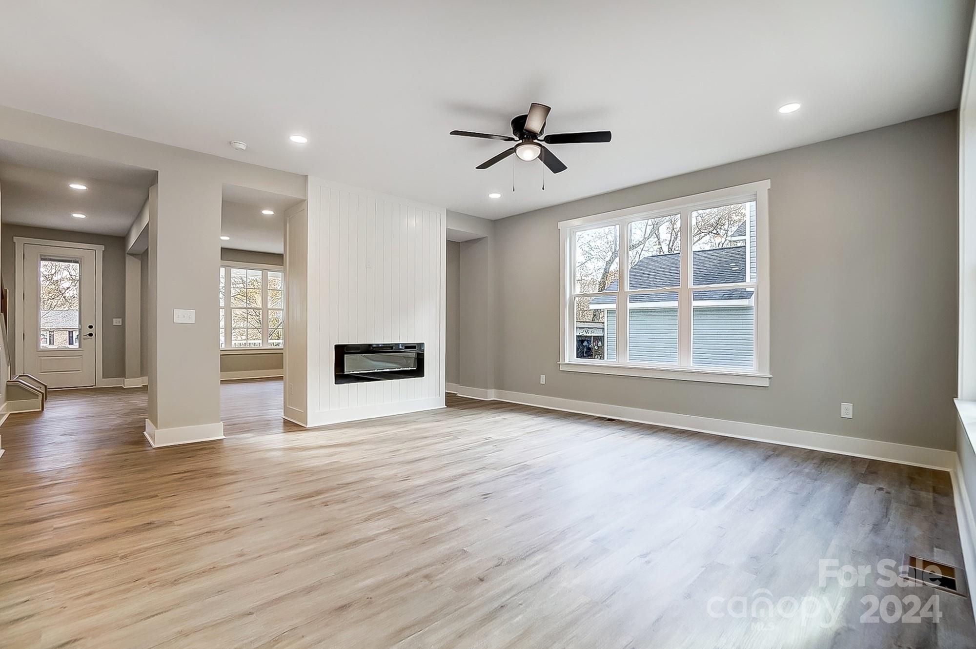 Vacant living room with wood floors, paneled fireplace partition, and large multi-pane window.