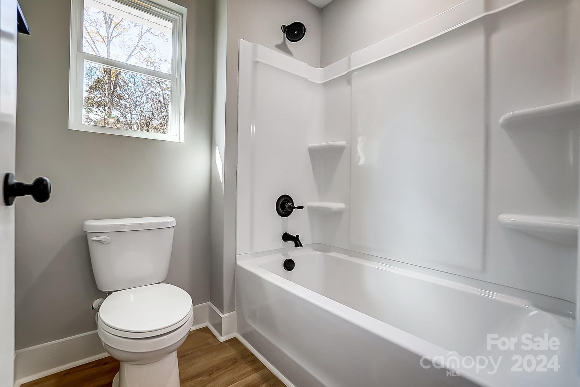 Bathroom with a white tub and shower, black fixtures, and a window above the toilet.