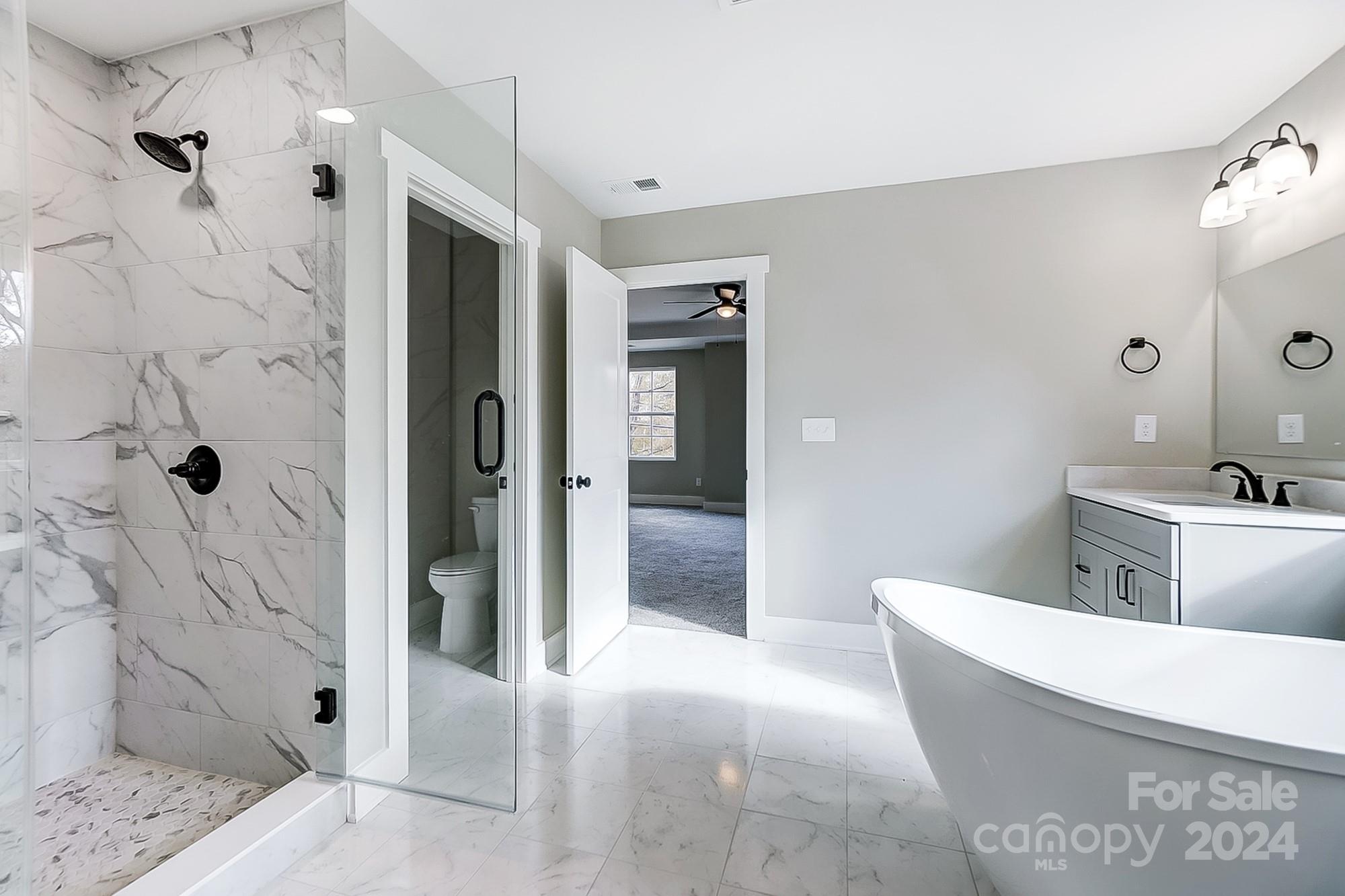 Bathroom with a freestanding tub, gray vanity, and glass-enclosed marble-look tiled shower.