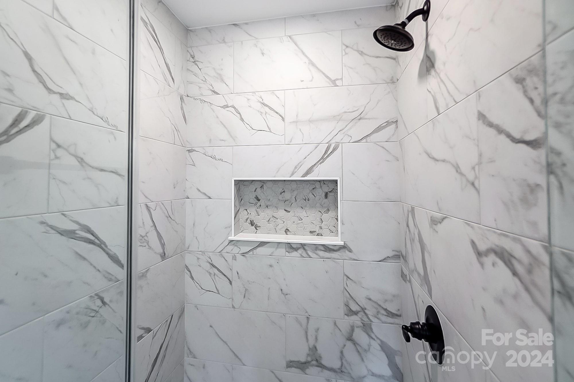 Walk-in shower with veined marble-look tile, a recessed niche, and matte black fixtures.