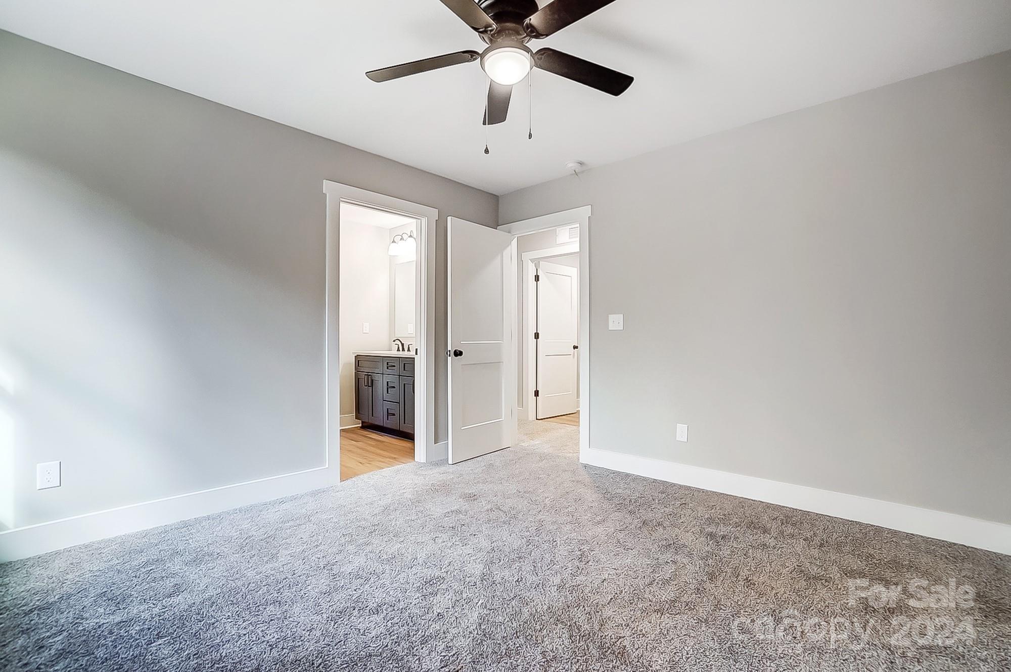 Empty carpeted bedroom with a ceiling fan and an open doorway to a bathroom vanity.
