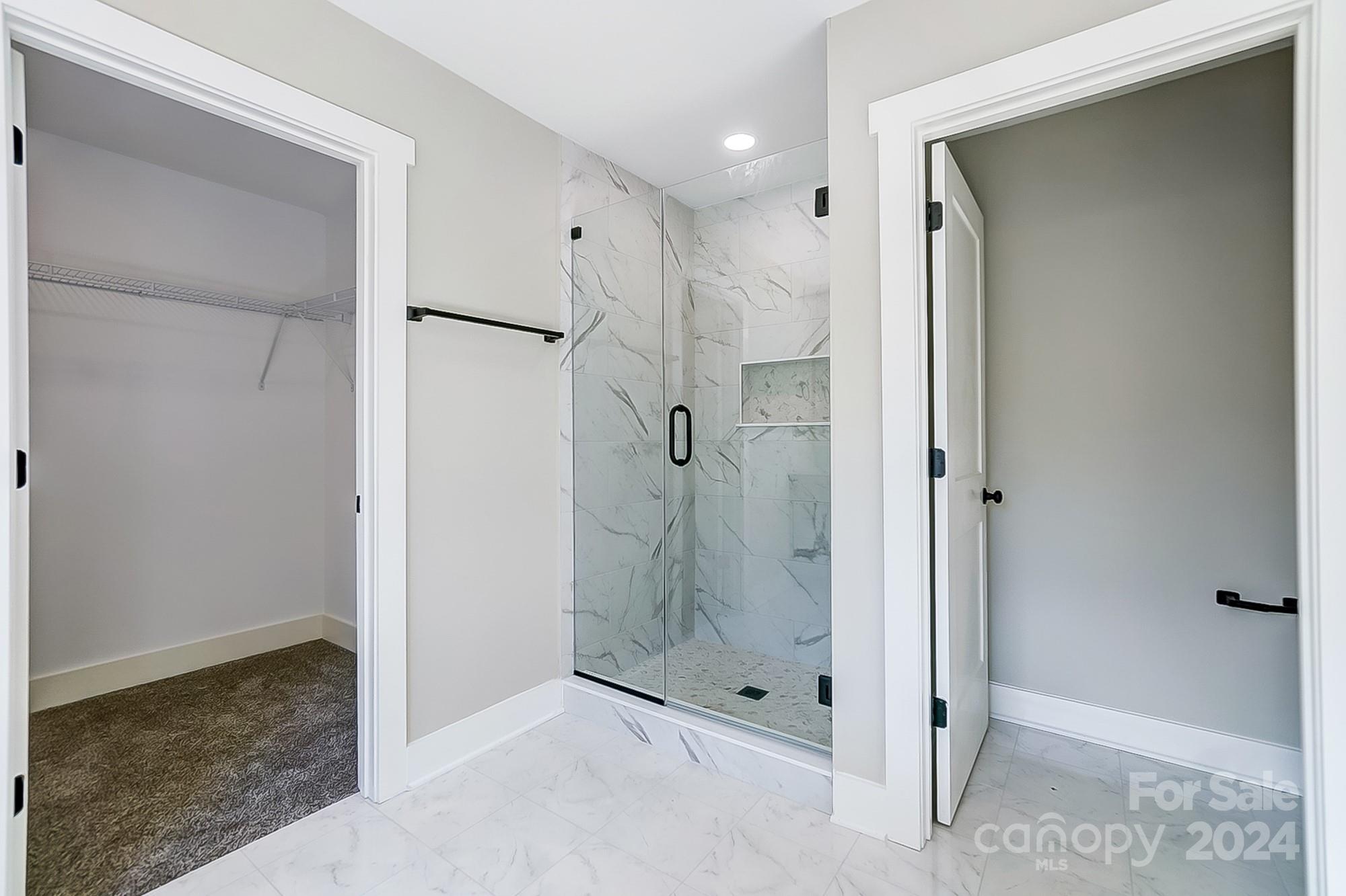 Bathroom with a glass-enclosed marble-look shower beside an empty carpeted closet.