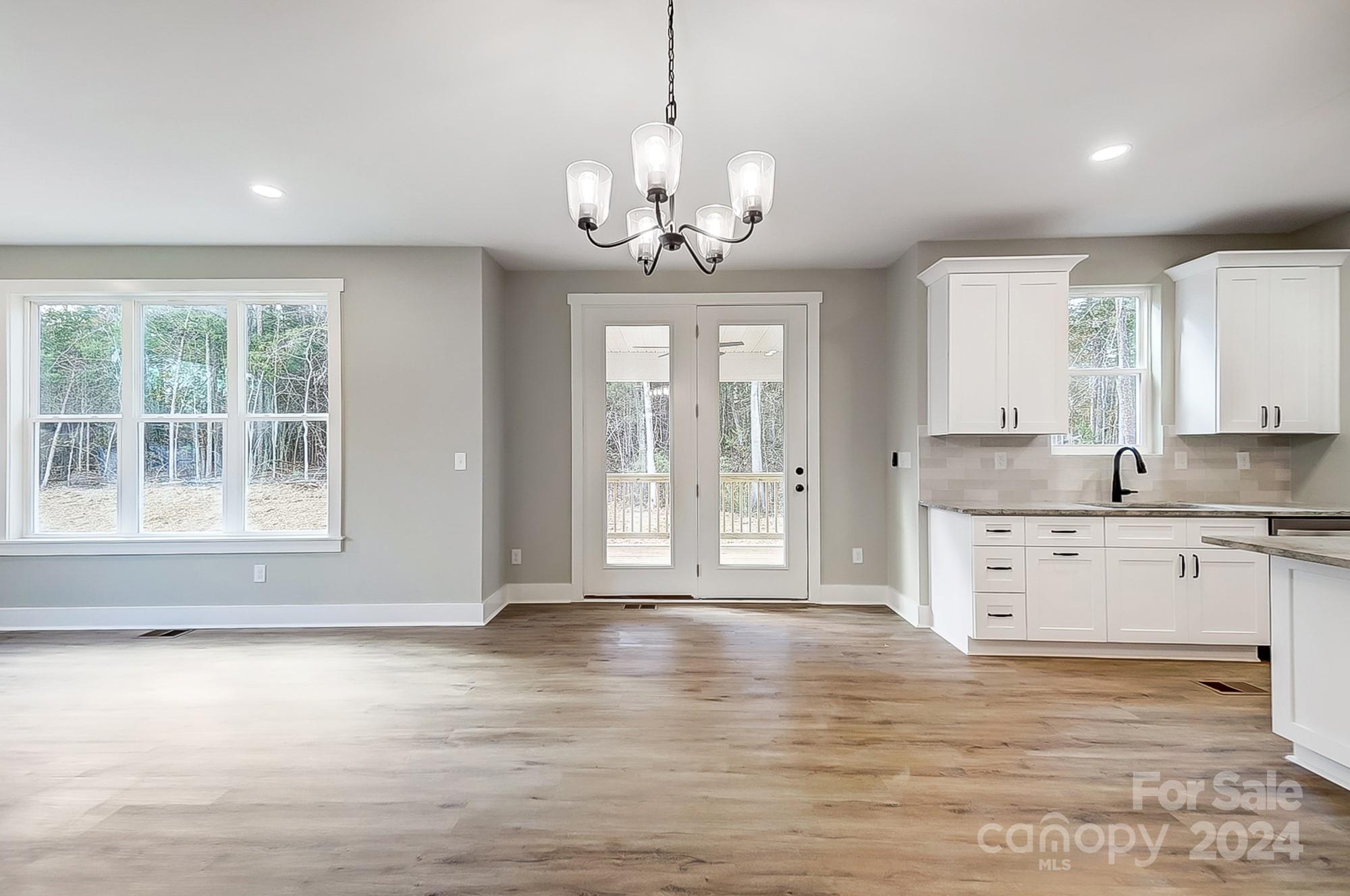 Vacant kitchen and dining area with white cabinets, wood-look floors, and windows overlooking trees.