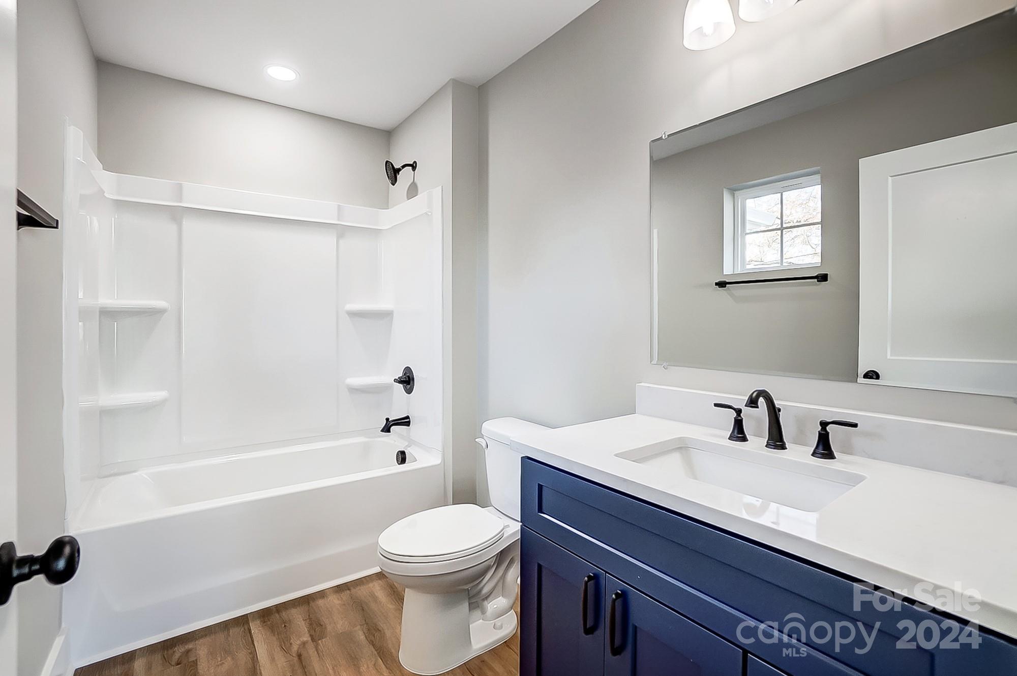 Bathroom with a white tub and shower, toilet, and navy vanity with black fixtures.