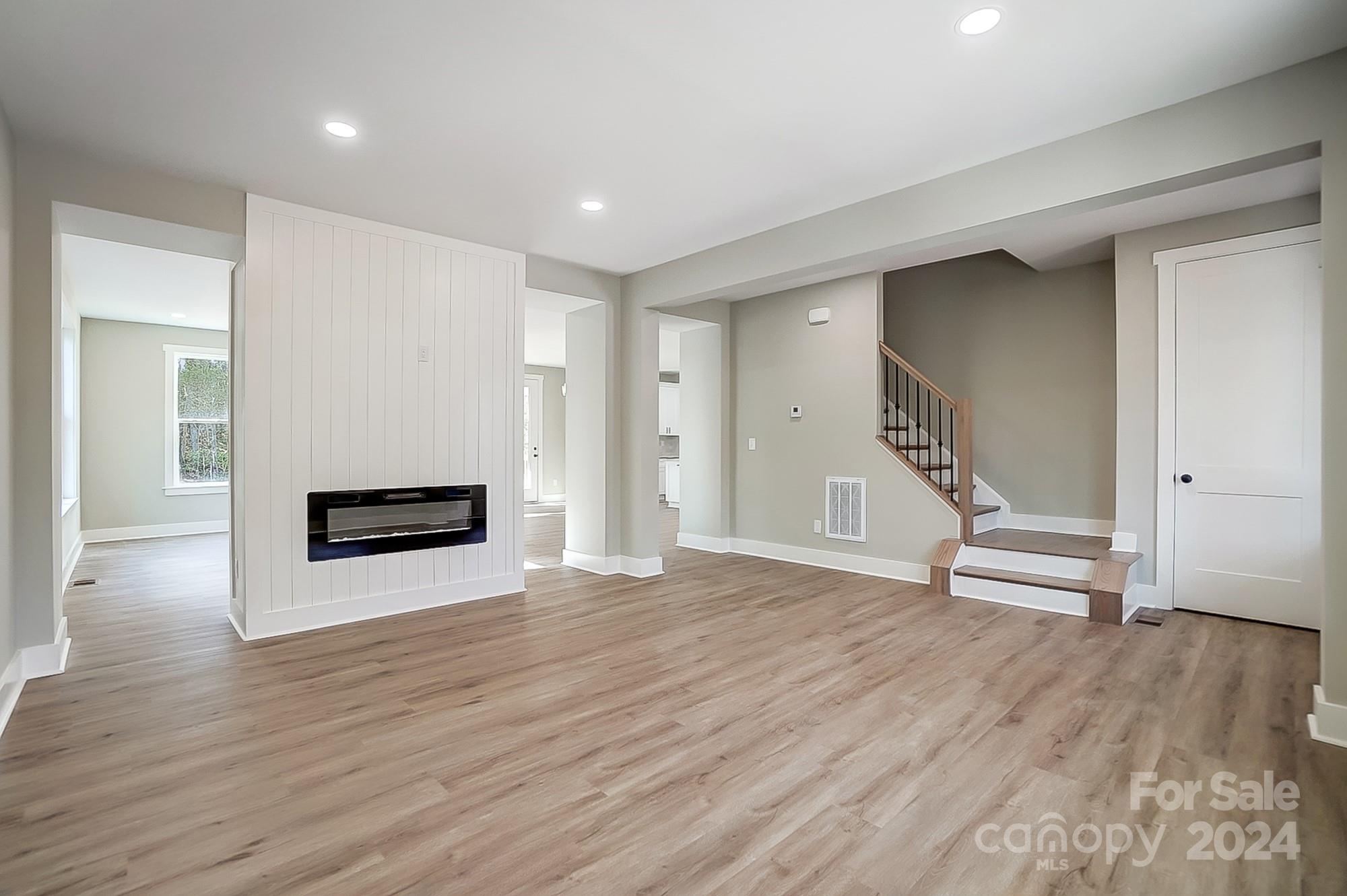 Vacant living room with a paneled fireplace divider, wide wood-look floors, and a staircase.