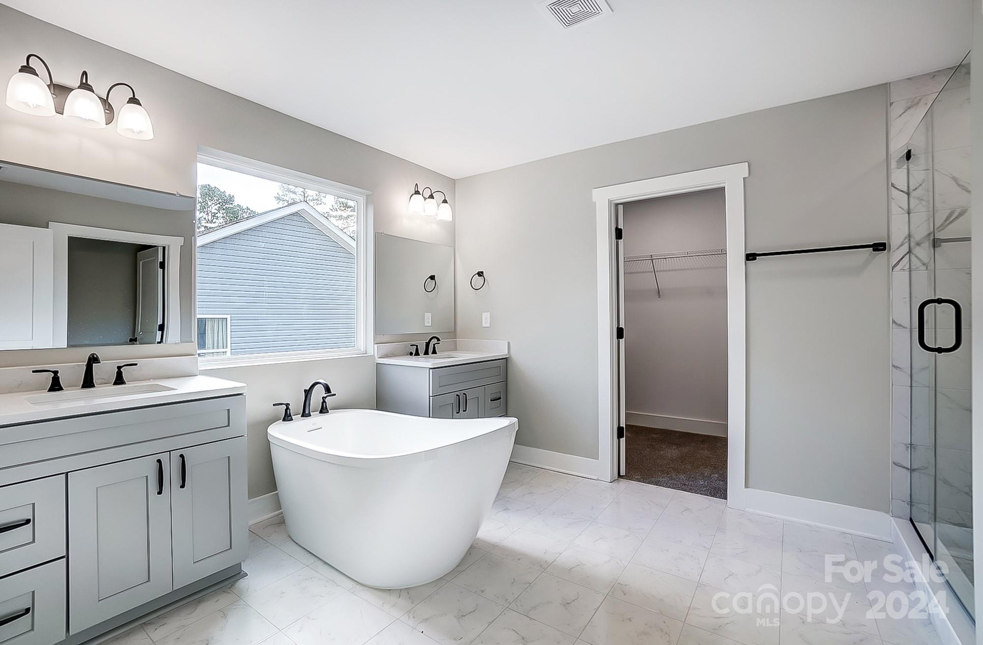 Bathroom with a freestanding soaking tub, gray double vanity, and glass-enclosed shower.
