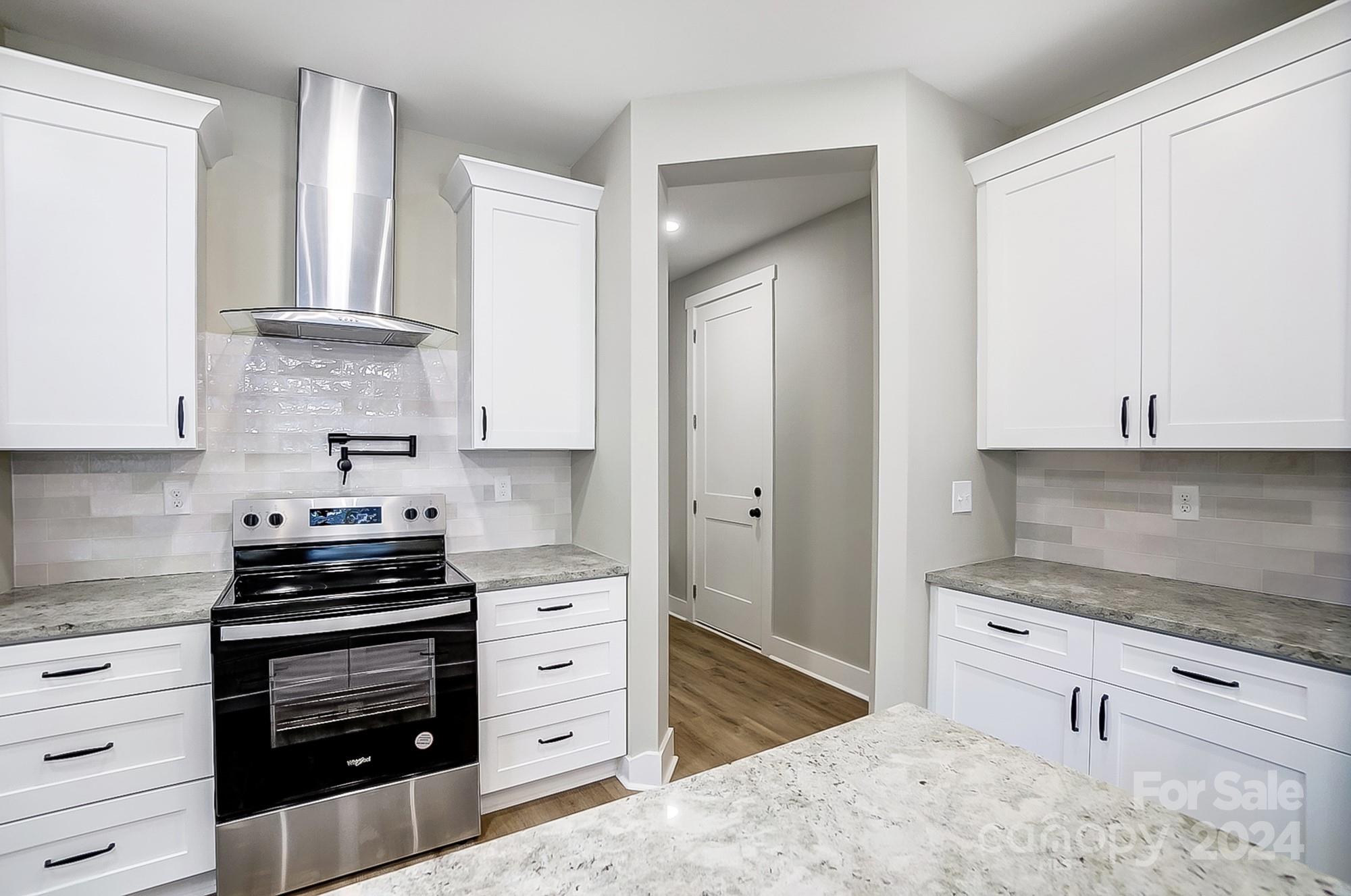 Bright kitchen with white shaker cabinets, gray stone counters, and a stainless steel range.