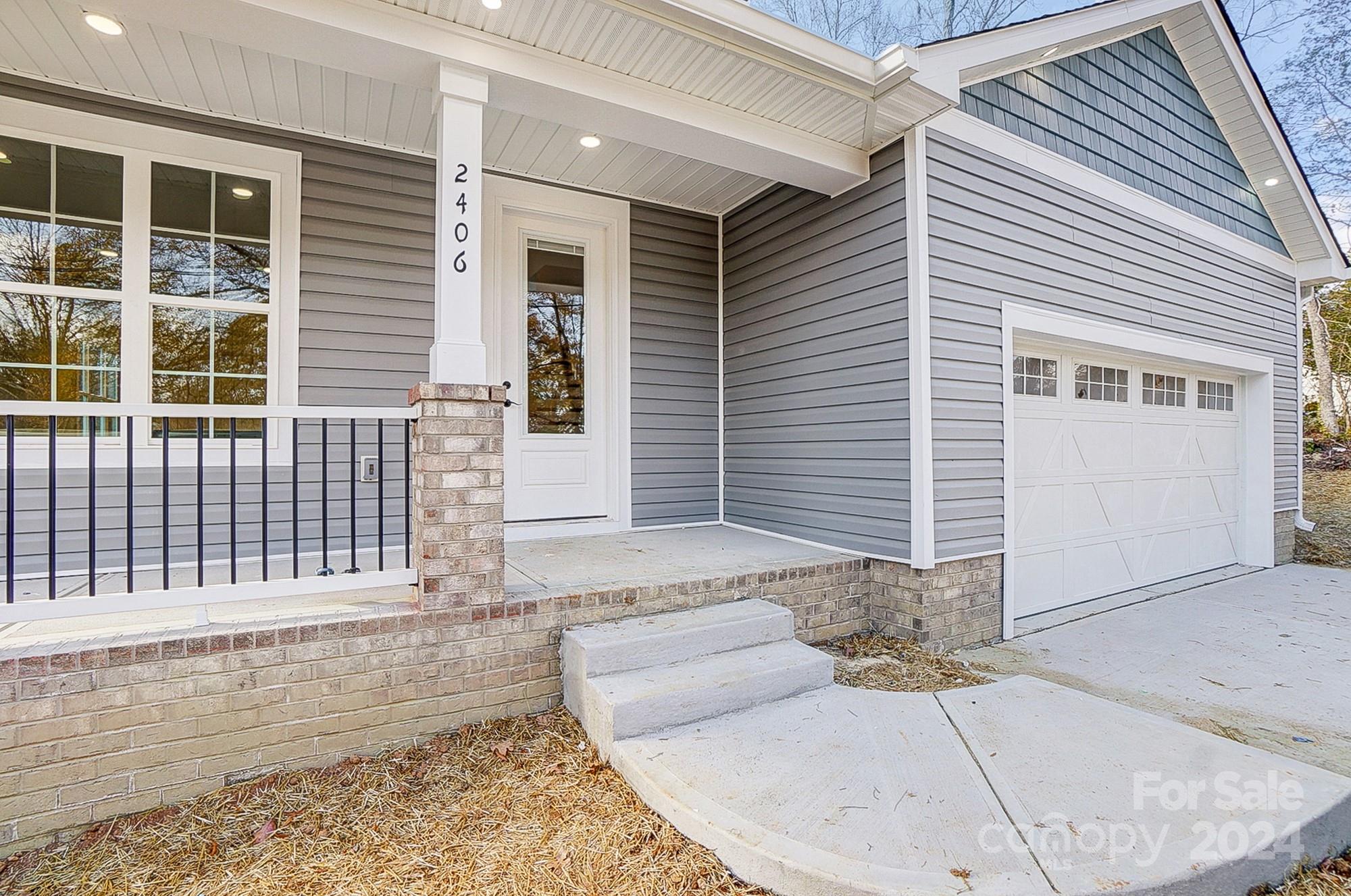 Gray-sided home entry with a covered brick porch, black railing, and attached white garage.