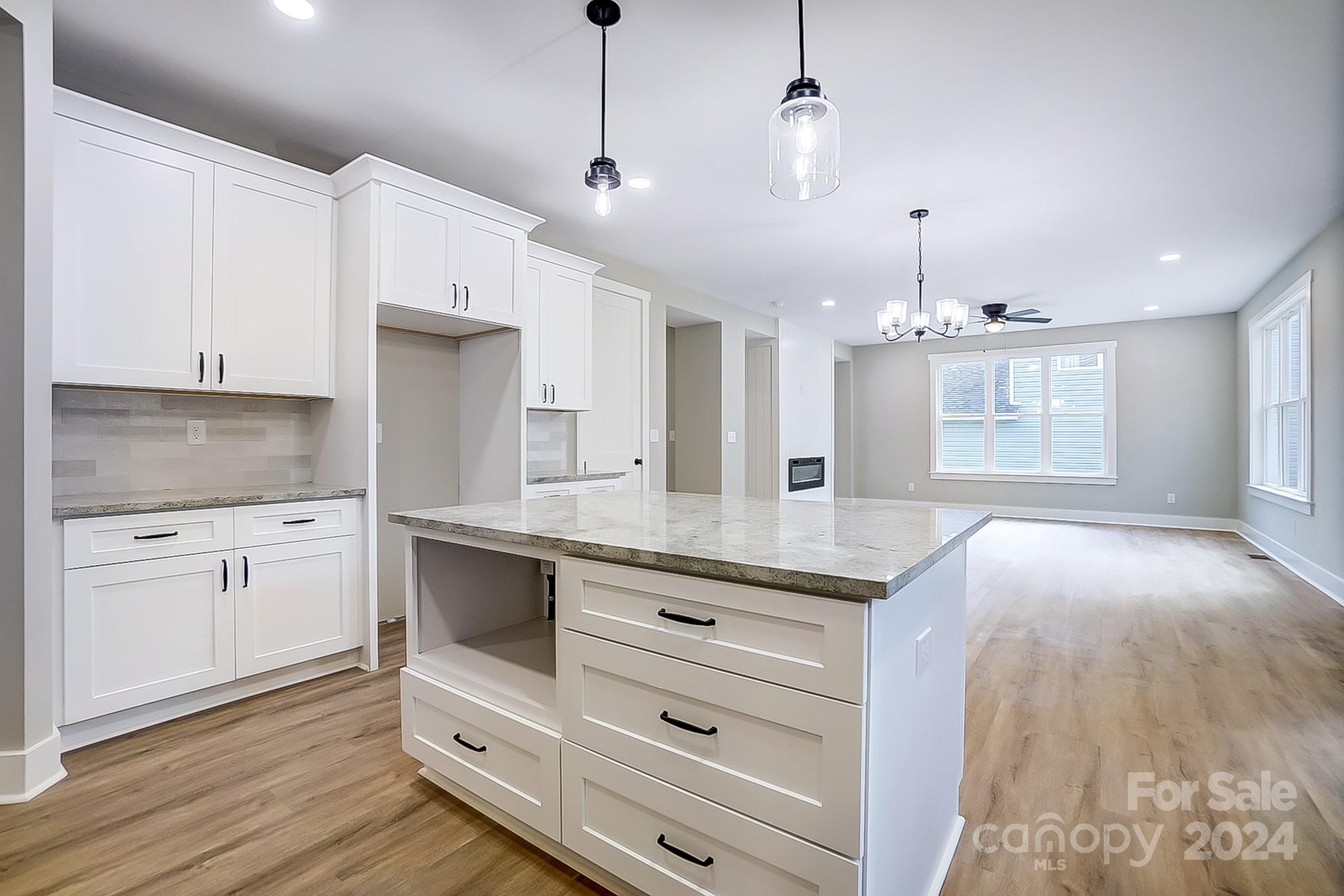 Vacant kitchen with white cabinets and a large stone-topped island opening to a bright living area.