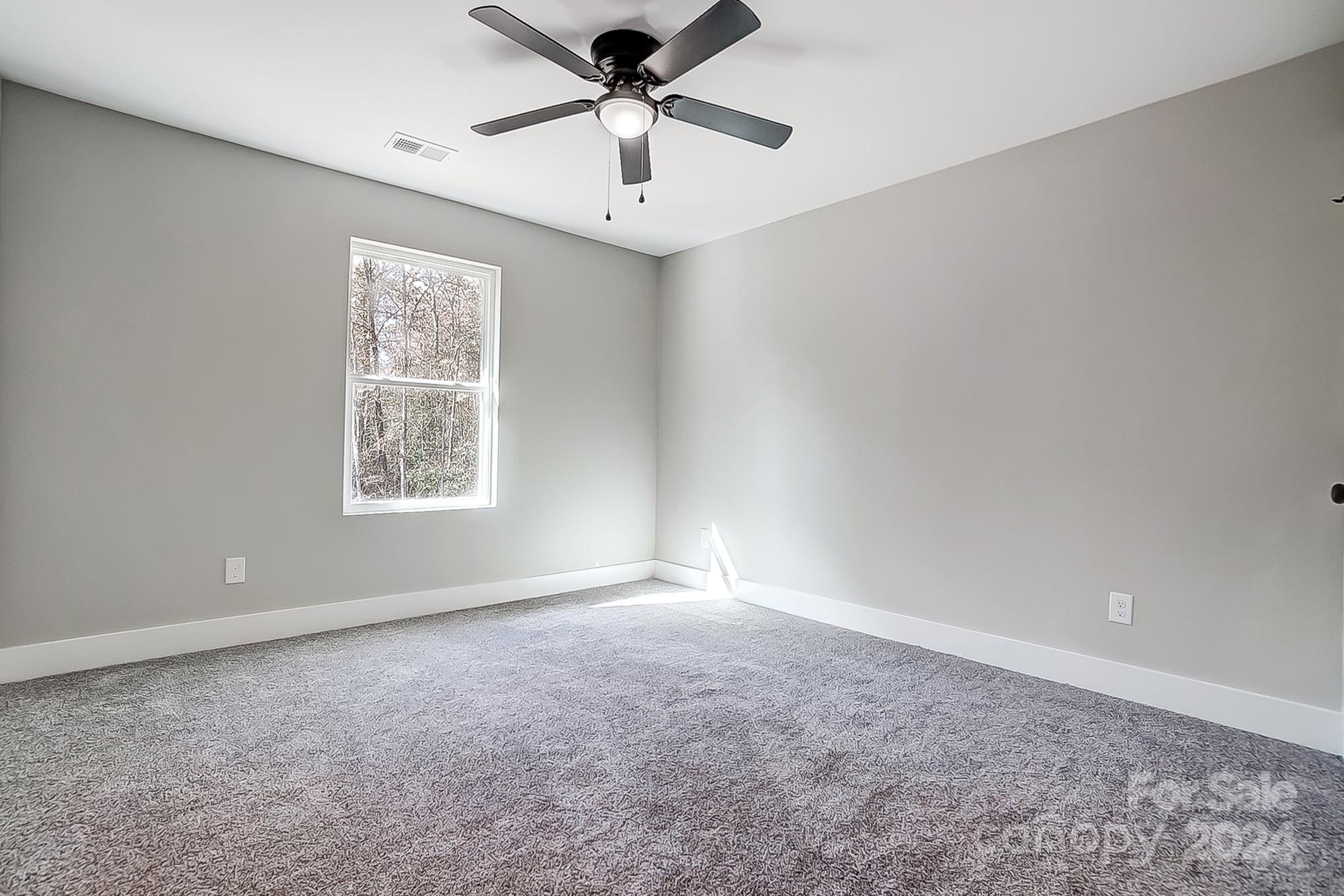Empty carpeted bedroom with gray walls, a window, and a ceiling fan.