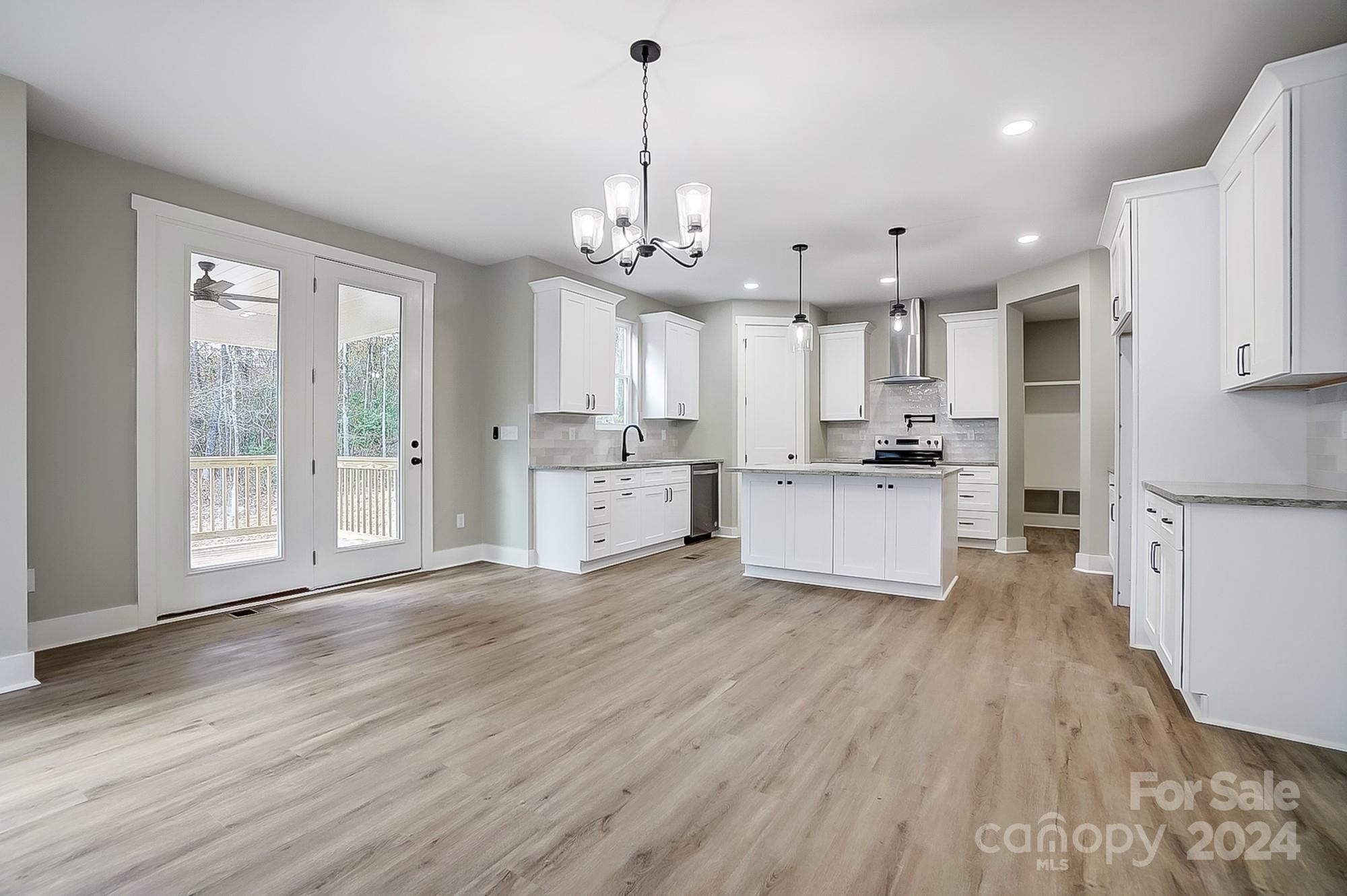 Bright kitchen with white cabinets, a central island, wood-look floors, and glass doors to a deck.