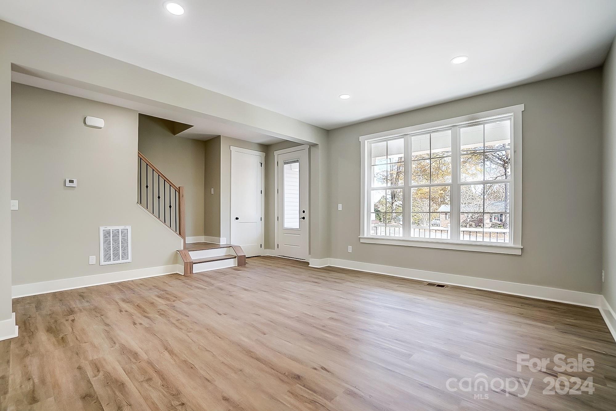 Empty living room with wood-look flooring, staircase, and large multi-pane window.
