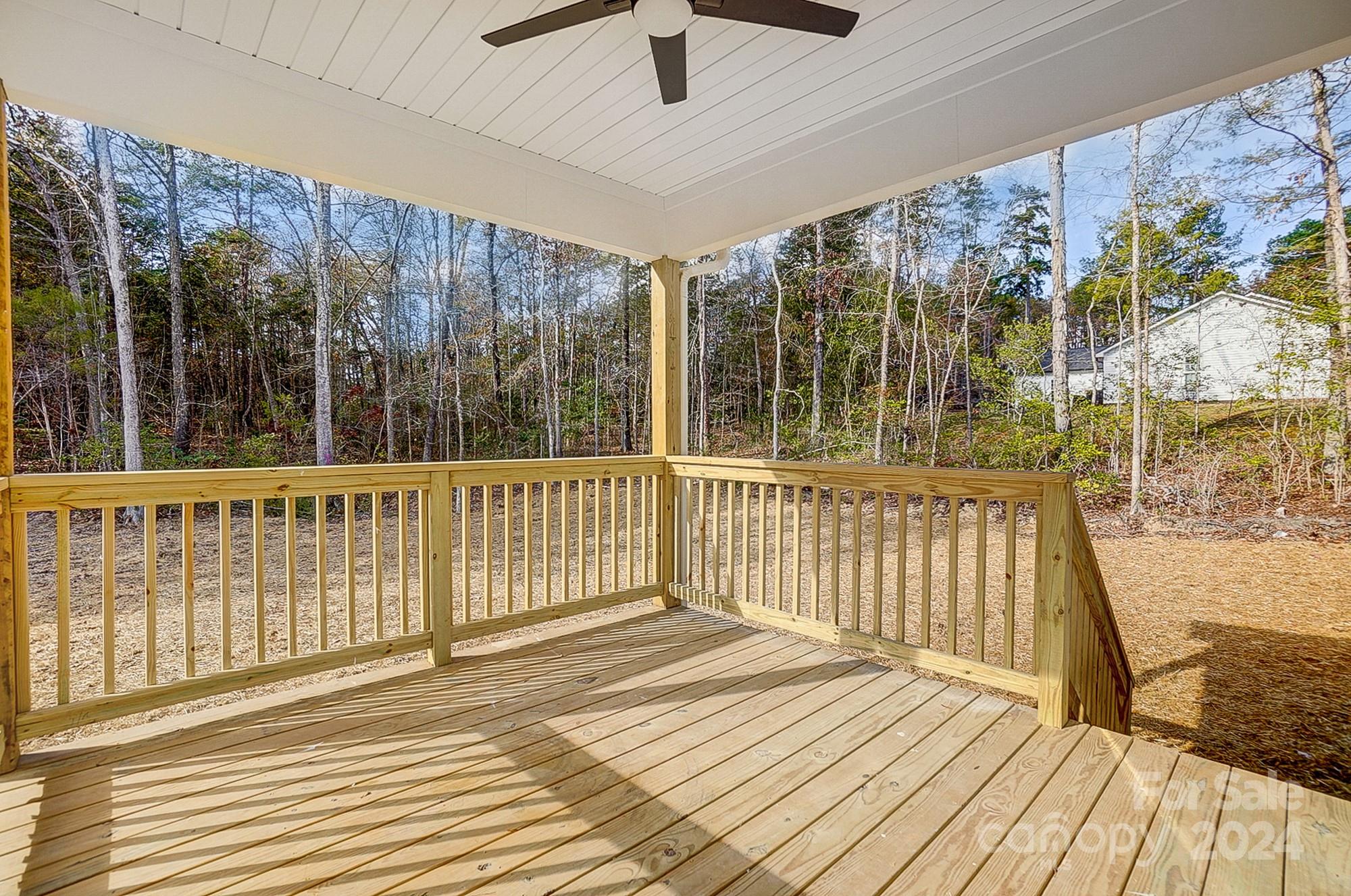 Covered wooden deck with railings and a ceiling fan overlooking a wooded yard.