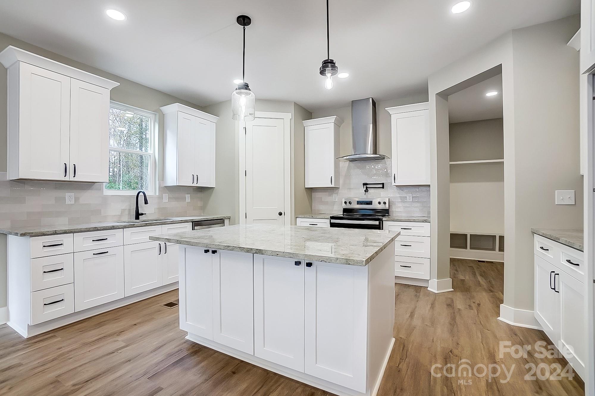 Kitchen with white cabinets, a large stone island, stainless range, and wood-look floors.