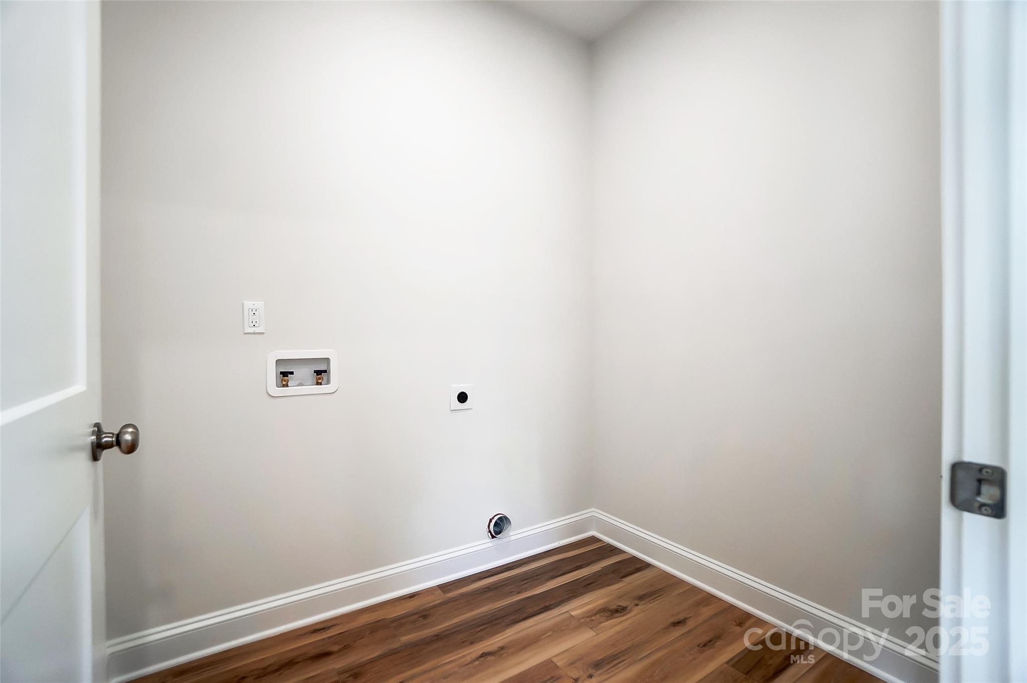 Empty laundry area with washer and dryer hookups and wood-look flooring.