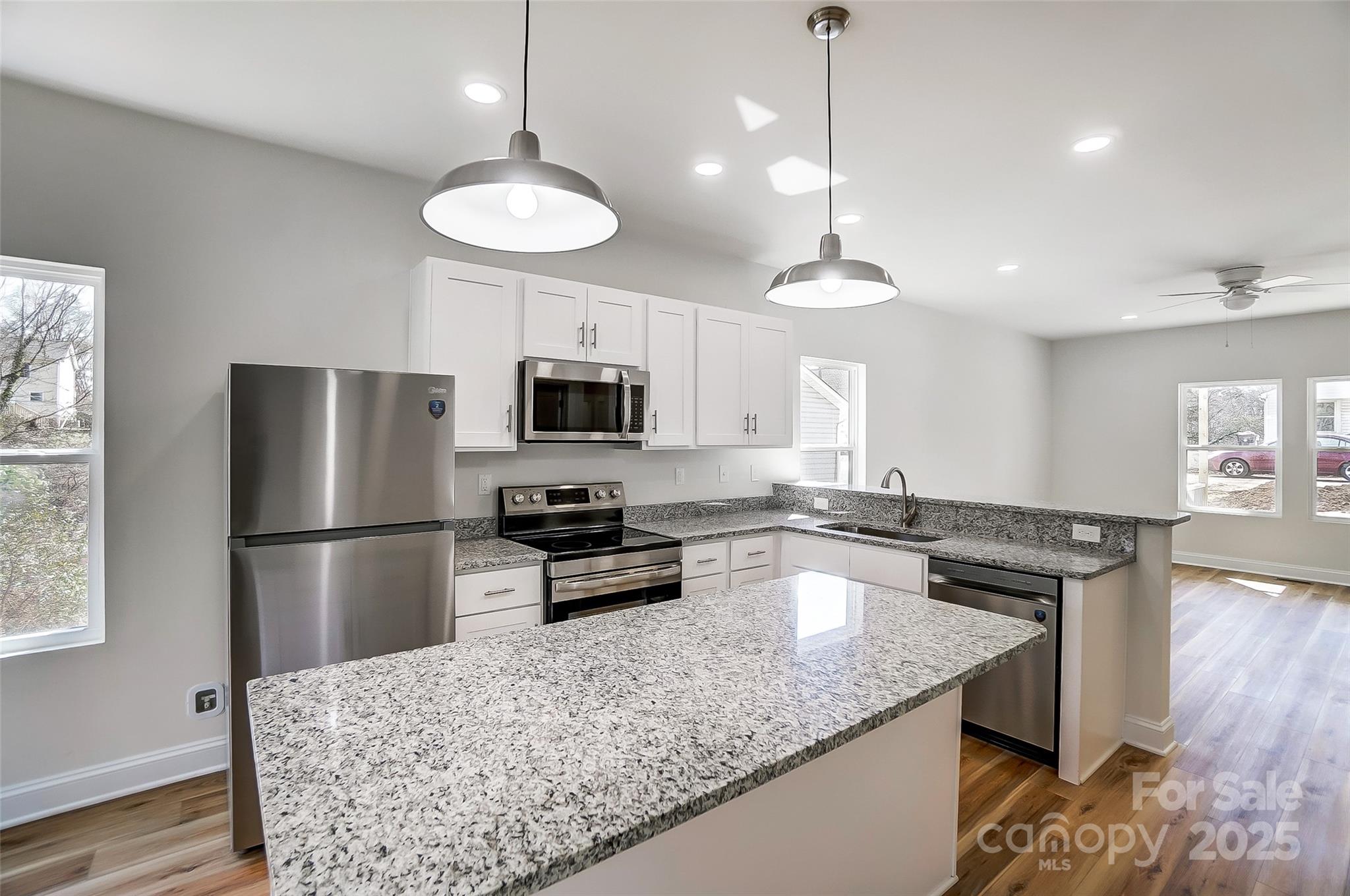 Vacant kitchen with white cabinets, stainless appliances, and a large granite island.