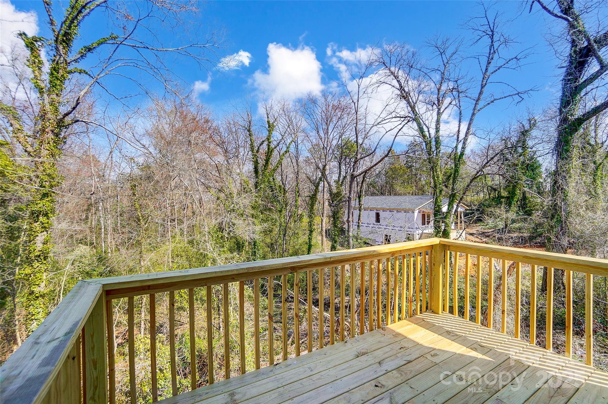 New wooden deck overlooking leafless woods and a house under construction.