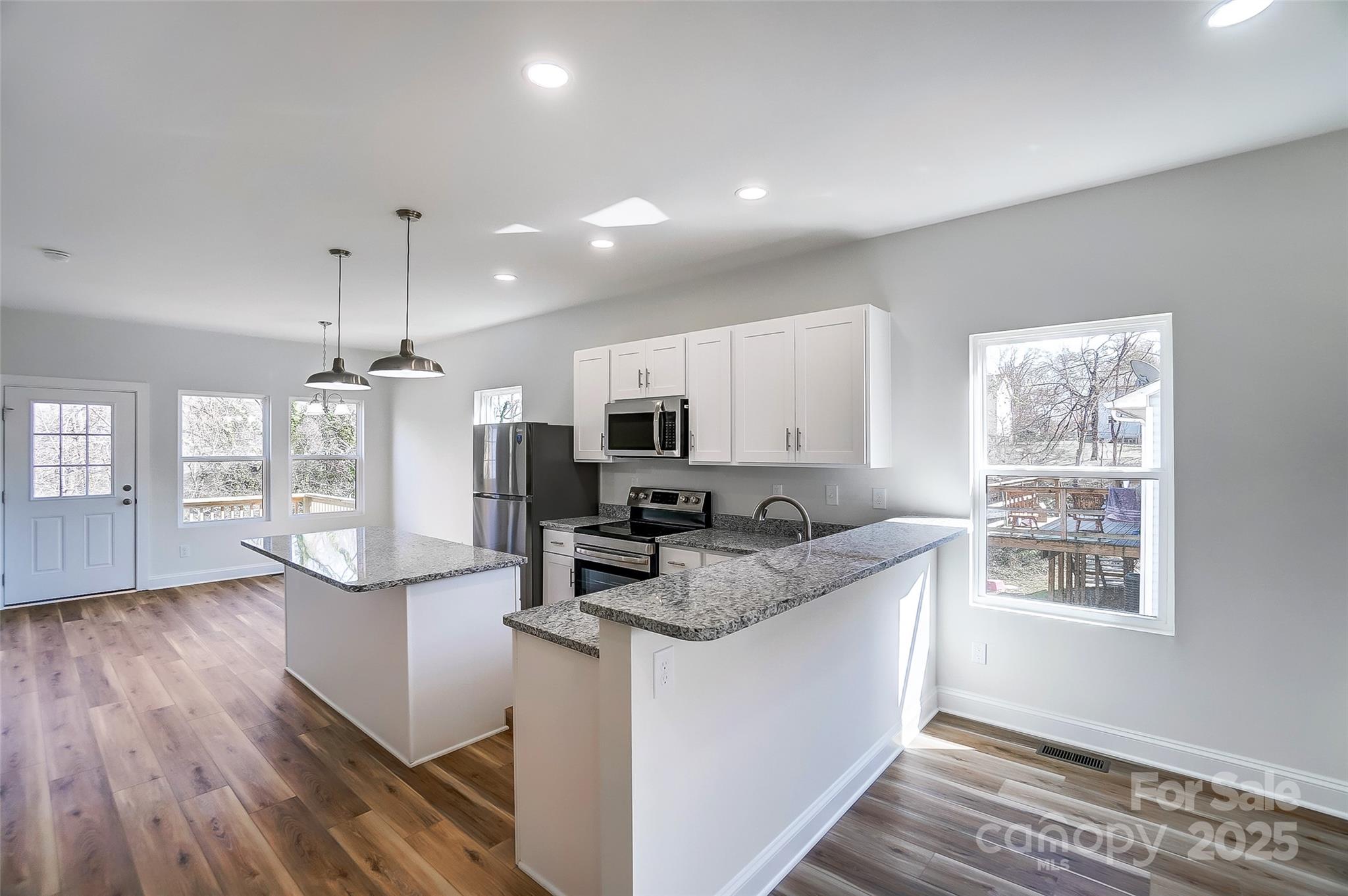 Bright vacant kitchen with granite counters, white cabinetry, stainless appliances, and a broad peninsula.