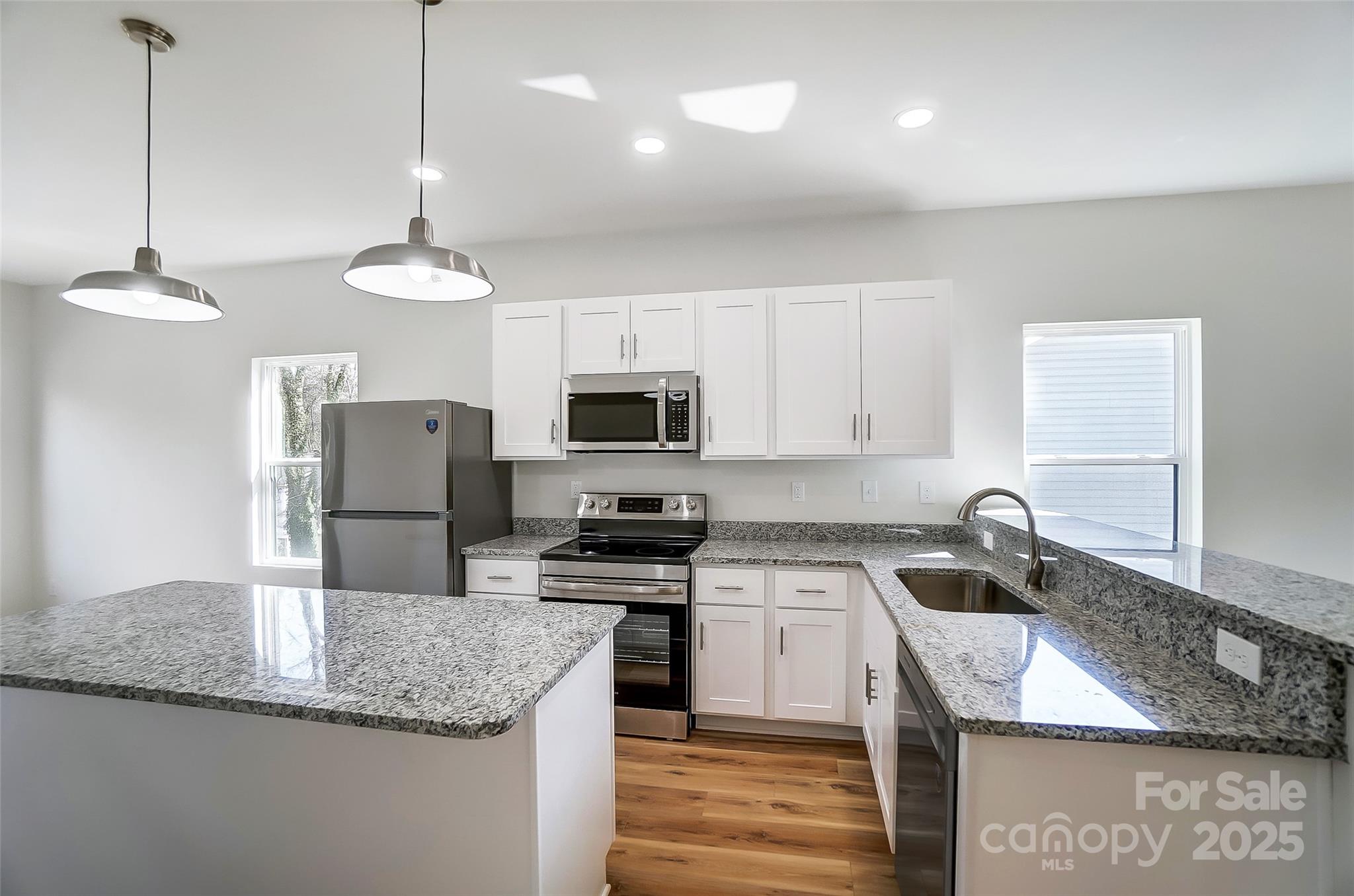 Bright kitchen with white cabinets, stainless steel appliances, and granite countertops wrapping around a large island.