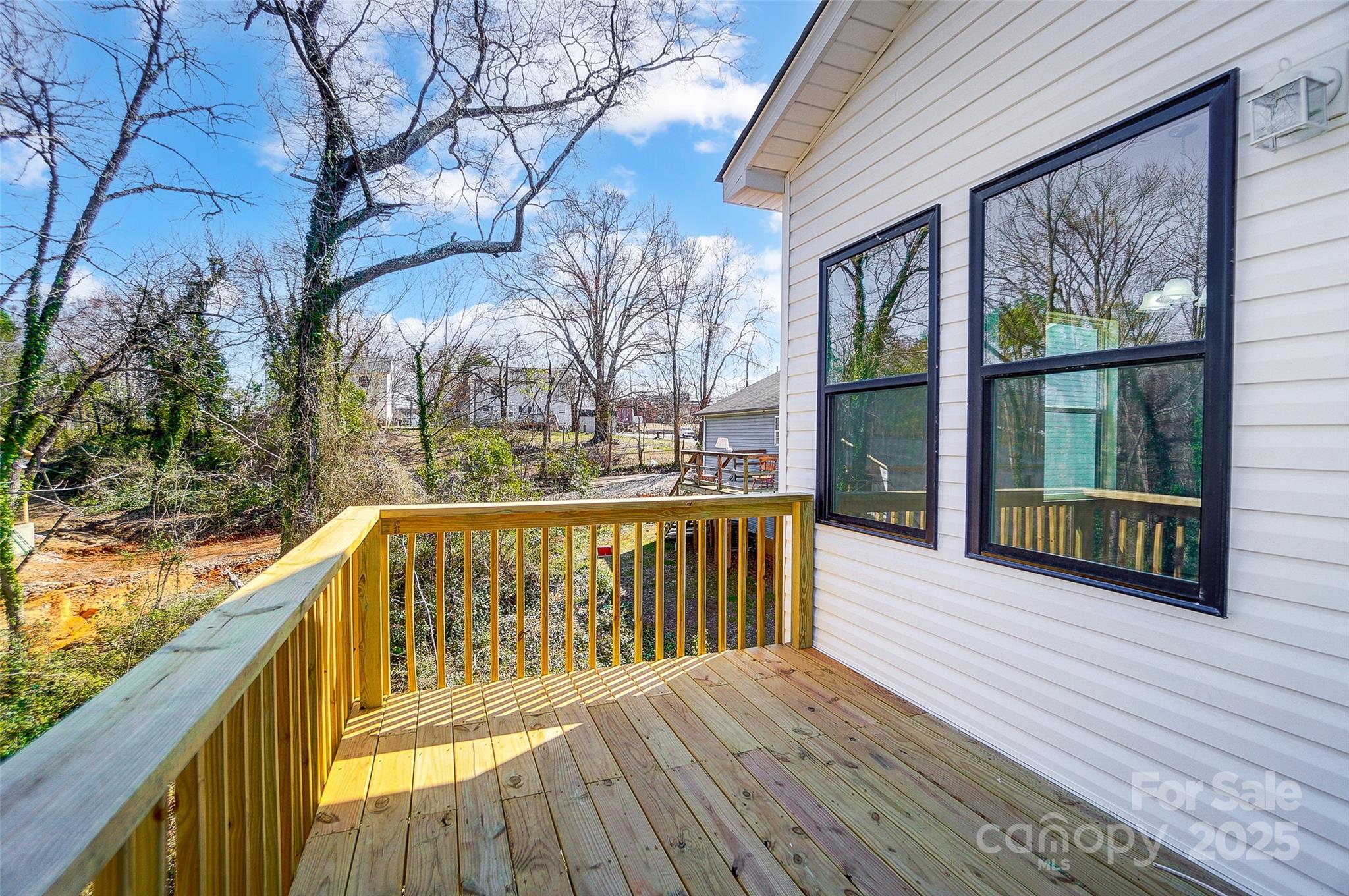 Wooden deck beside white siding, with black-framed windows and a wooded yard beyond.