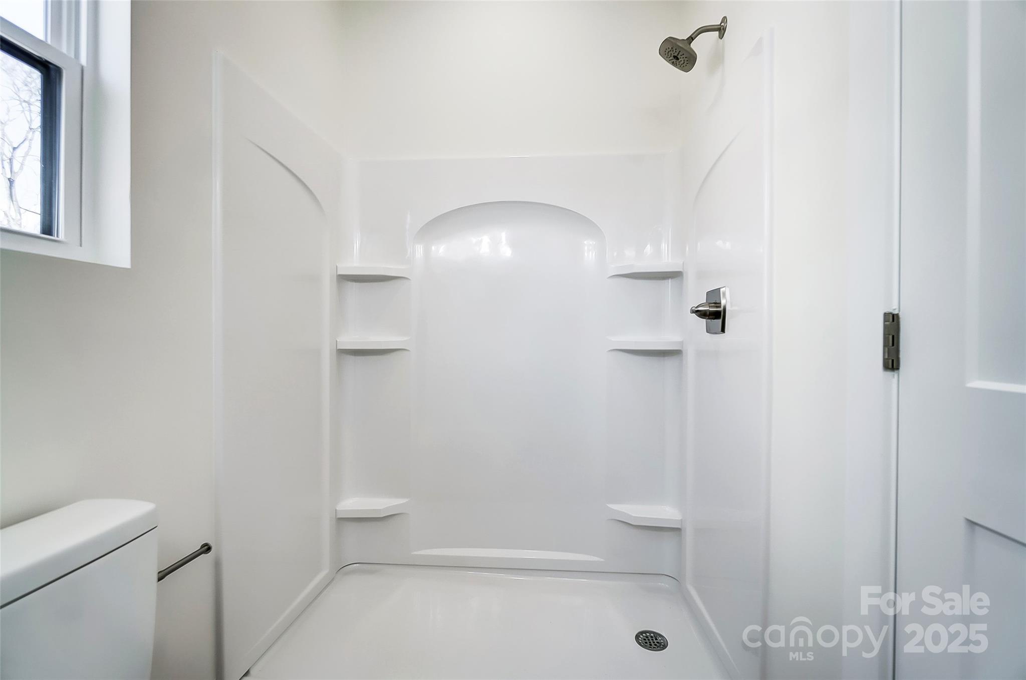 White walk-in shower with built-in shelves and chrome fixtures beside a small window.