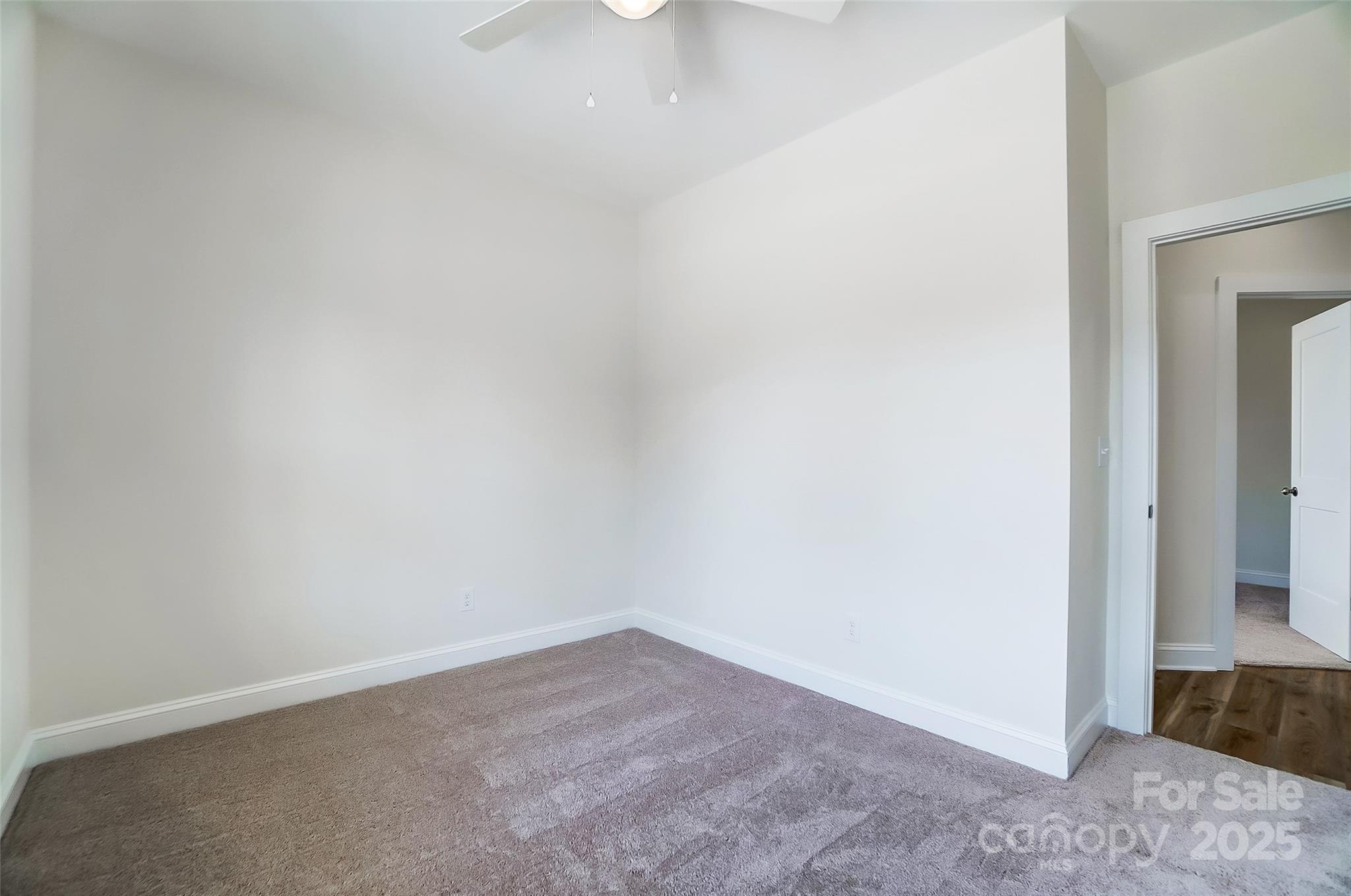 Empty carpeted bedroom with a ceiling fan and open doorway to the hall.