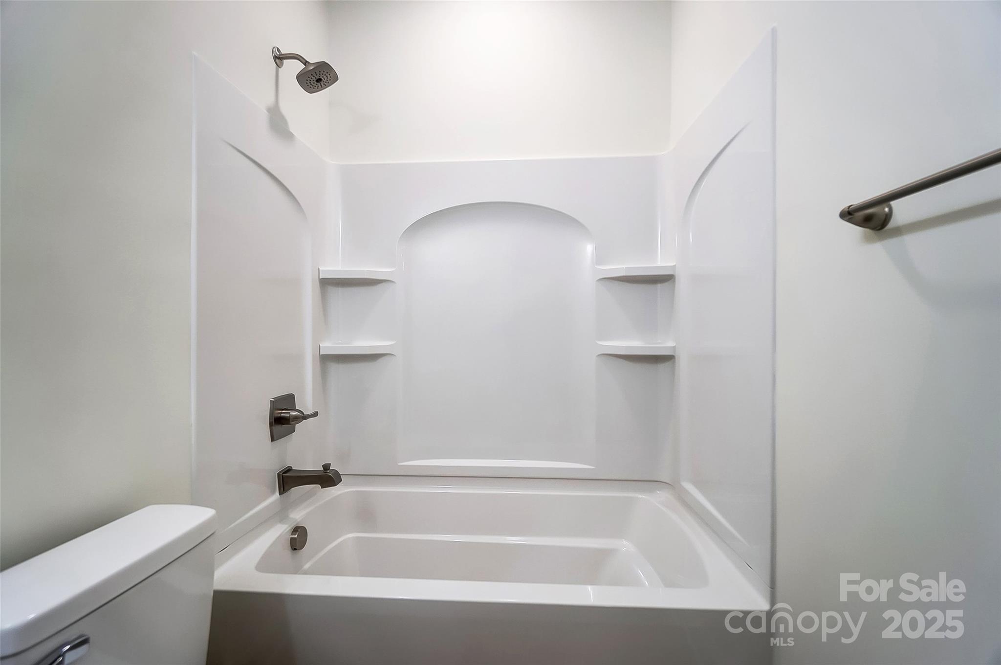 White bathtub and shower with built-in shelves and dark metal fixtures.