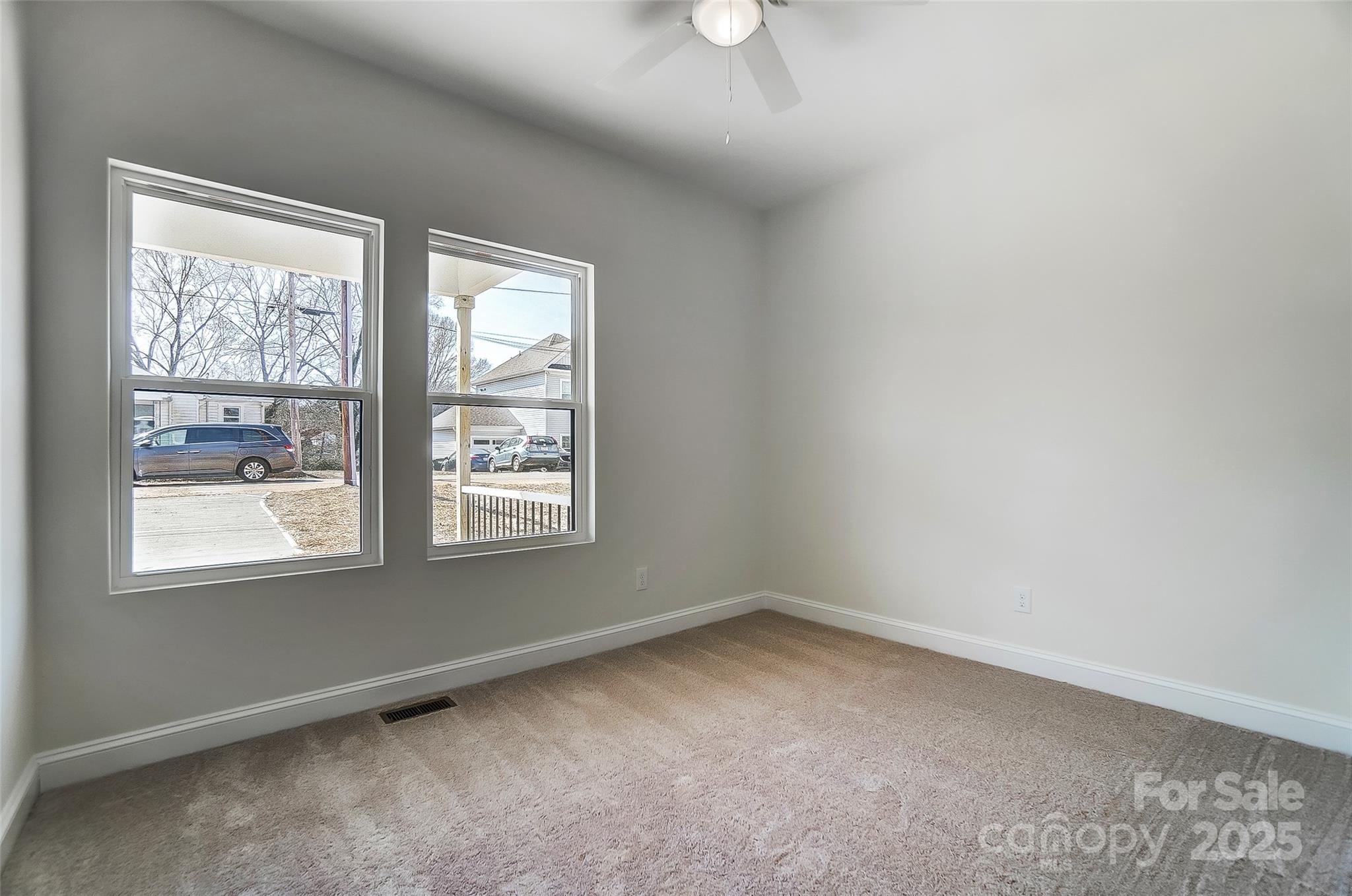 Empty bedroom with beige carpet, two windows, and a ceiling fan.