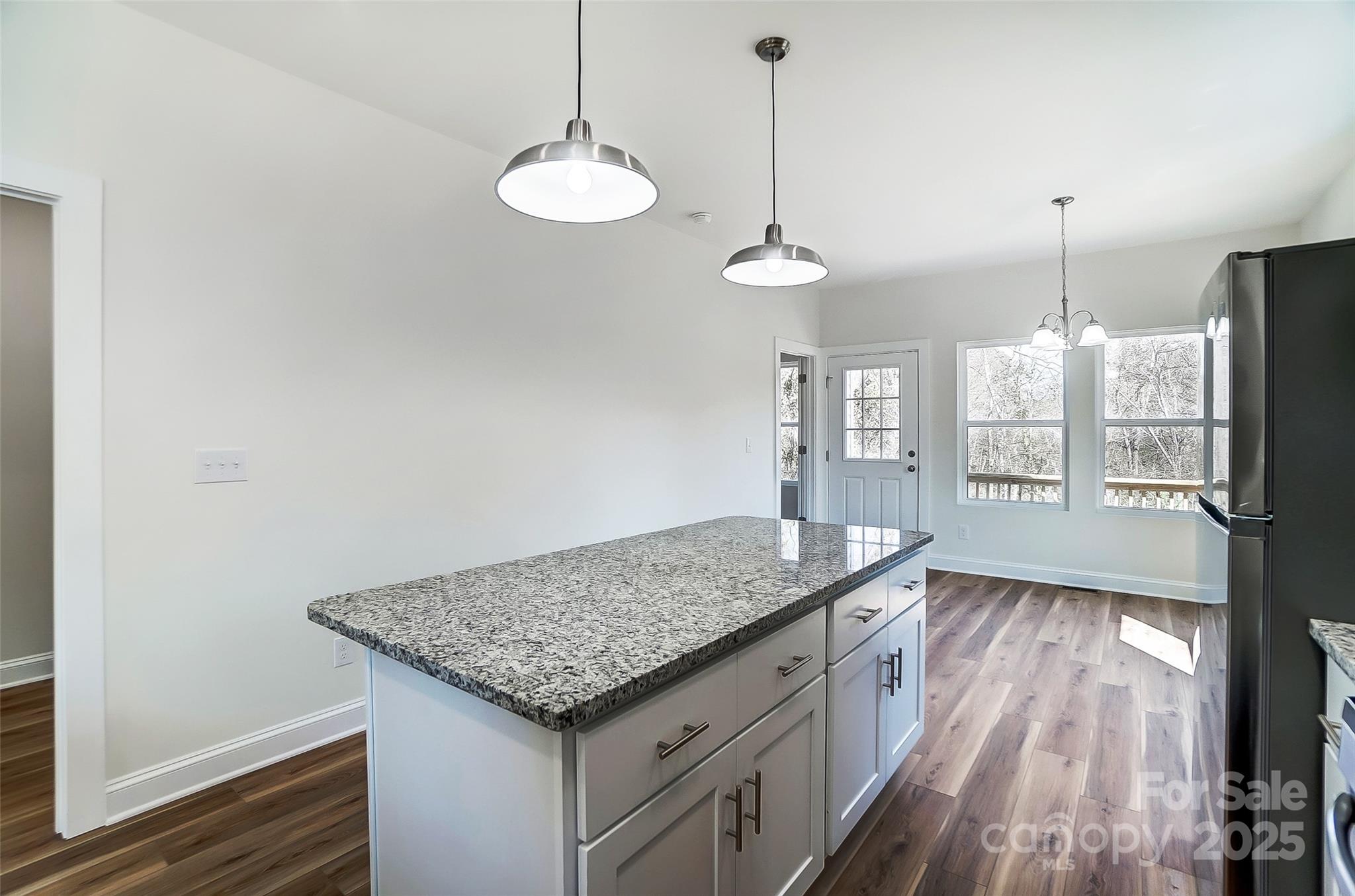 Bright kitchen with a granite island, white cabinetry, pendant lights, and windows beside a glazed exterior door.