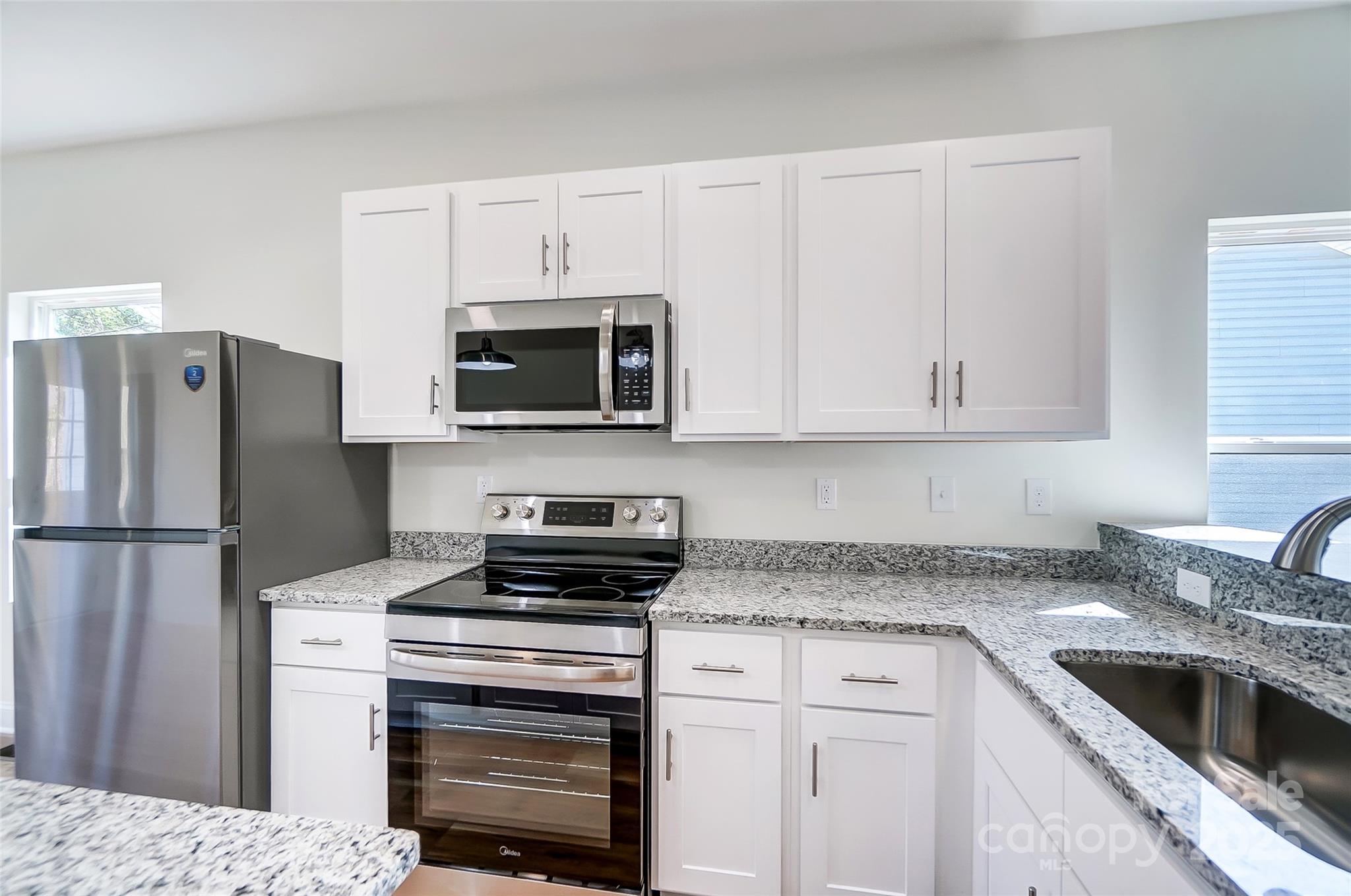 Kitchen with white cabinets, granite counters, stainless appliances, and a corner sink.
