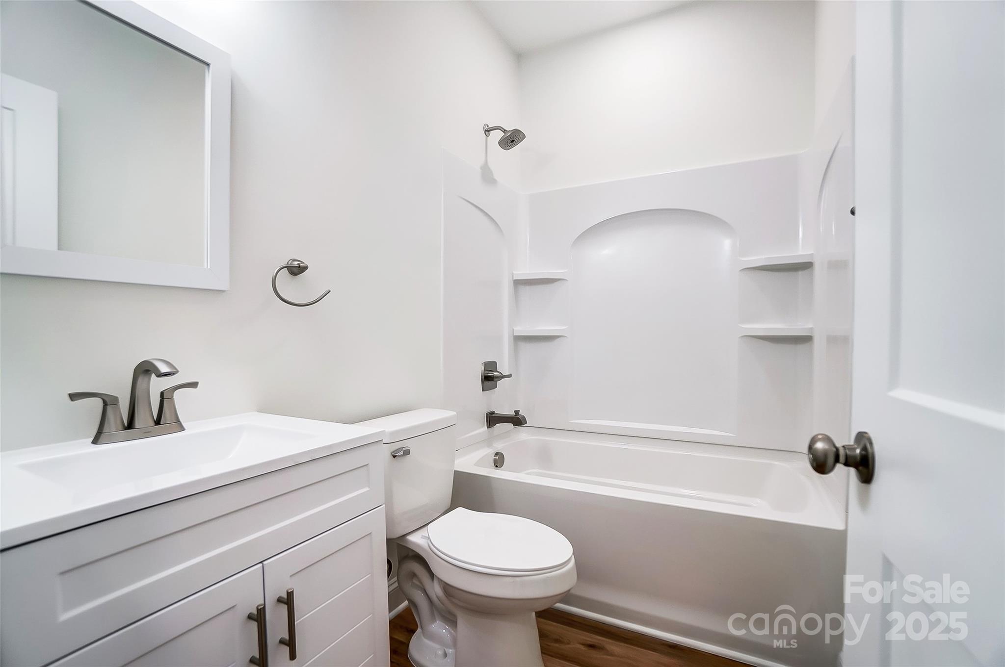 White bathroom with a vanity, toilet, and bathtub featuring built-in shelving.