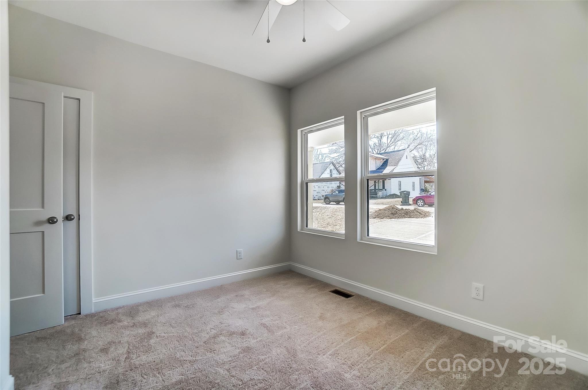 Empty carpeted room with two windows and a ceiling fan.